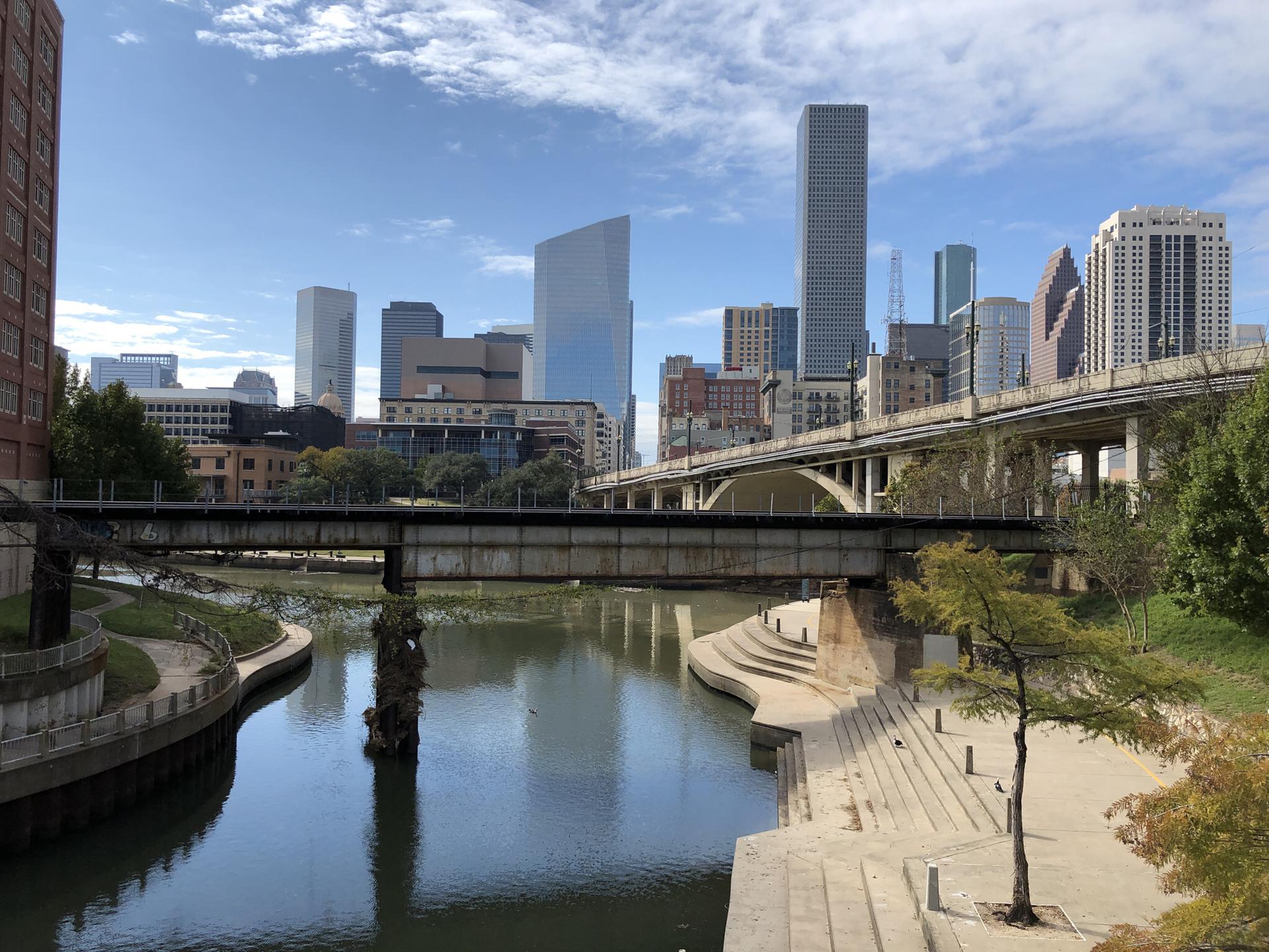 Urban skyline with a river, multiple bridges, and concrete riverbanks under clouds.