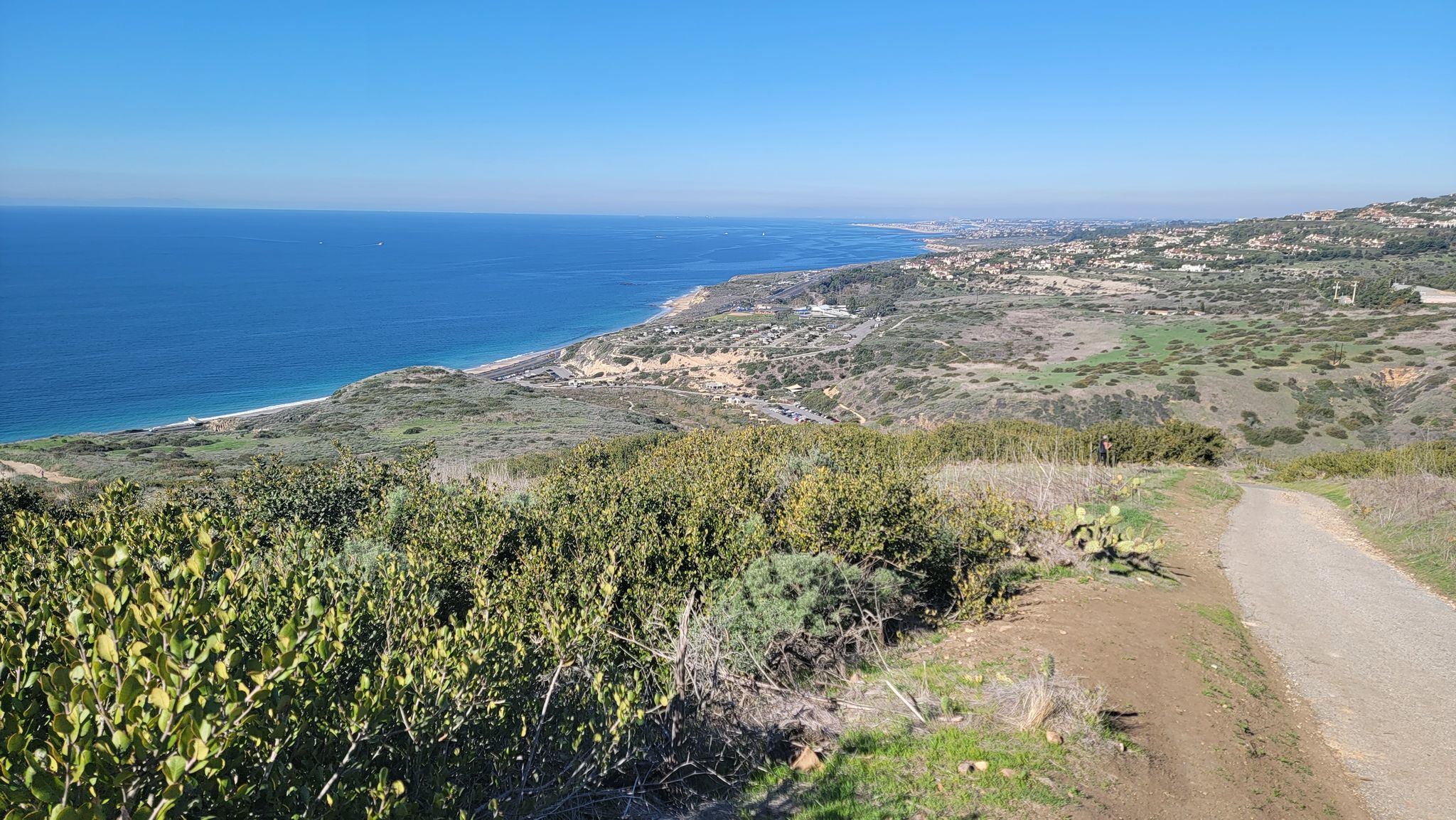 A wide view of the ocean coastline with green hills and a dirt path. - El Moro Canyon to Moro Ridge Loop