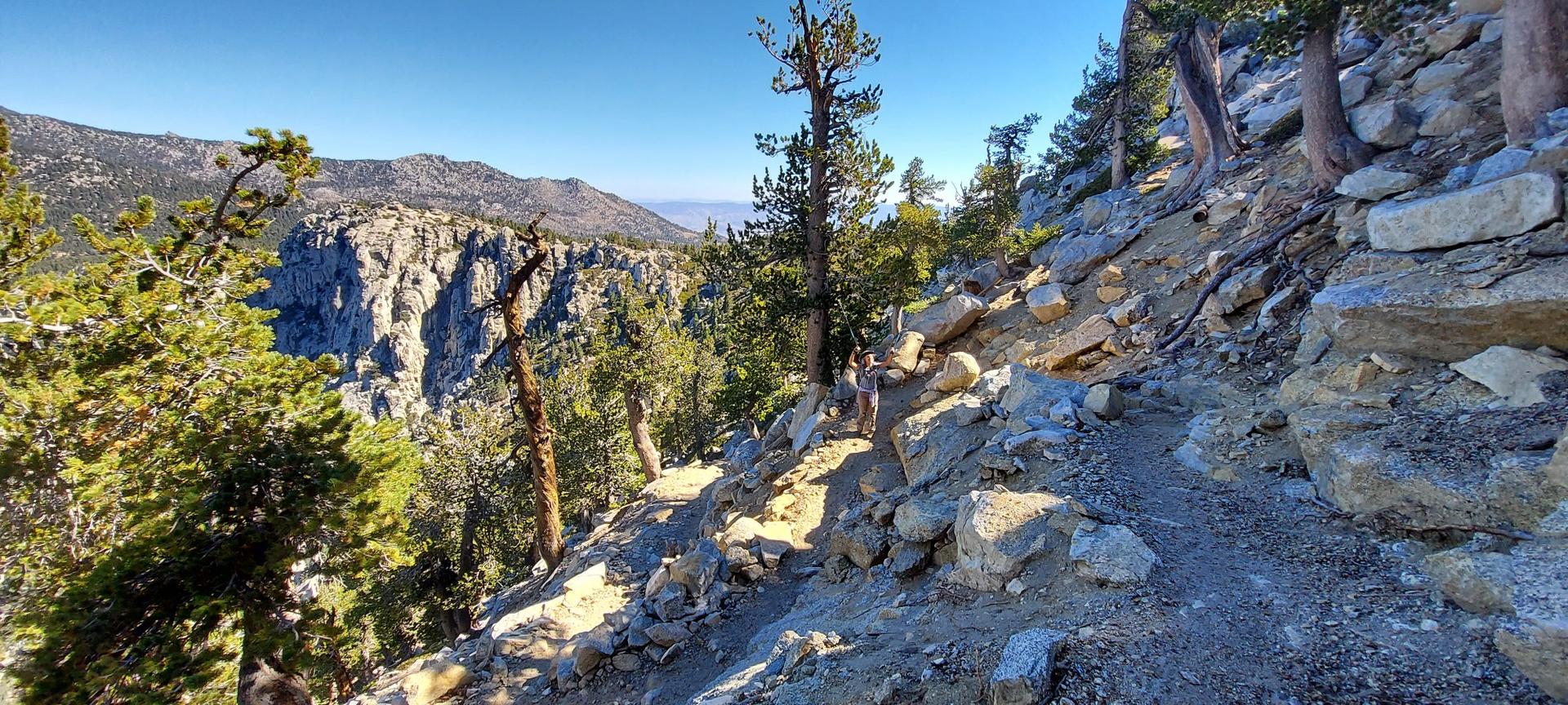 A winding mountain trail on a steep, rocky slope under a clear sky.