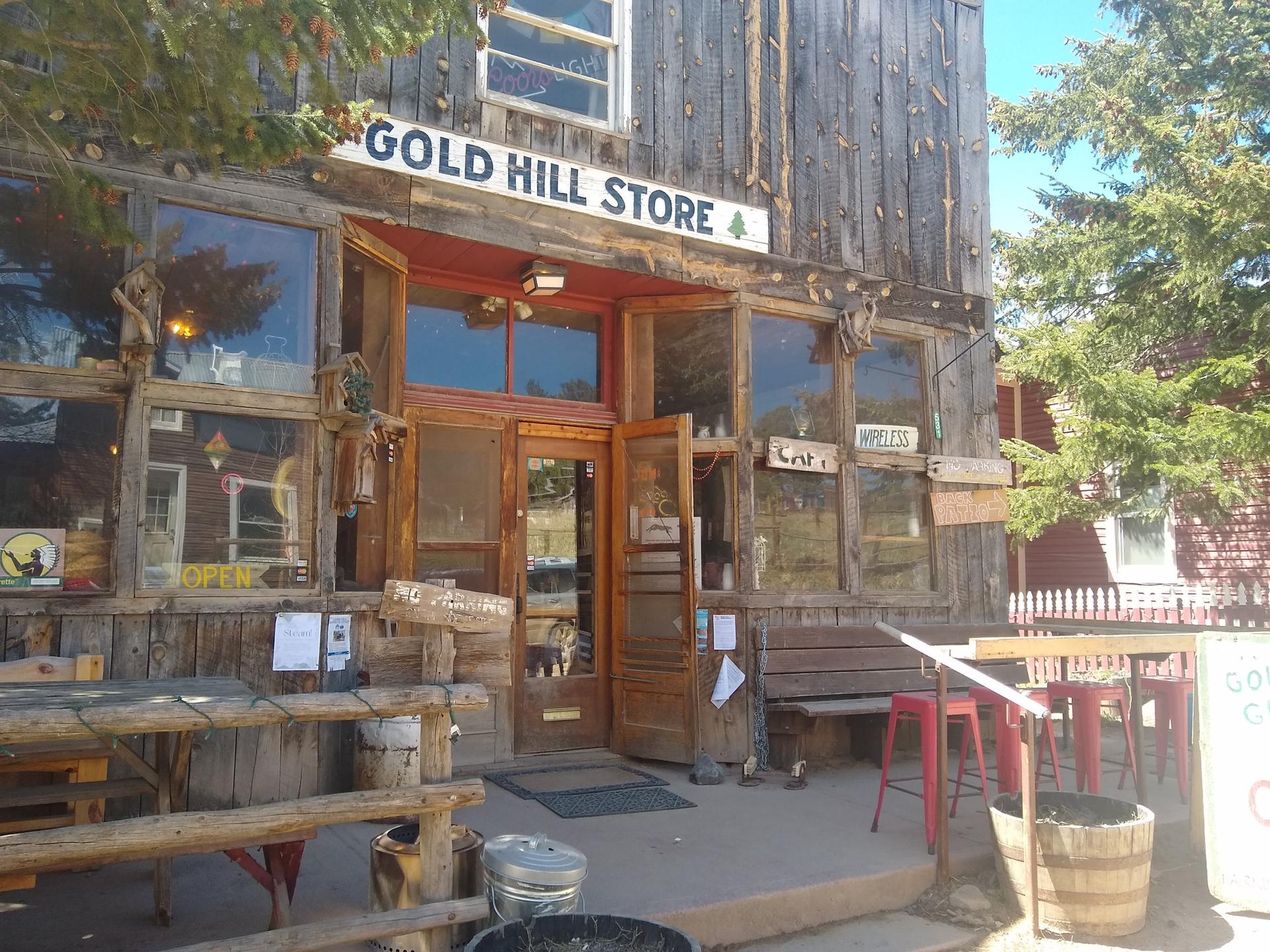 A rustic wooden store building with a sign and outdoor seating in daylight.