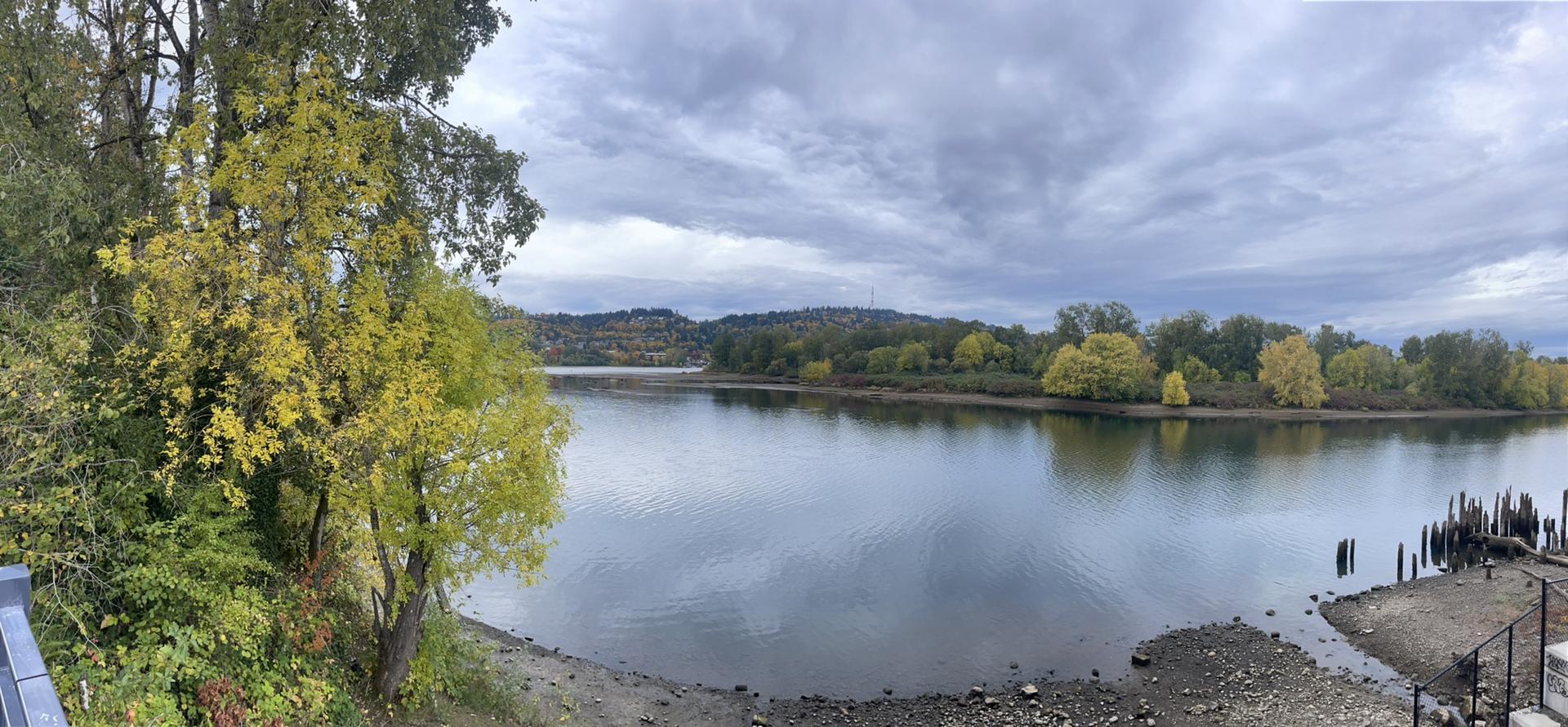 Panoramic river view with autumn trees and cloudy, dramatic sky.