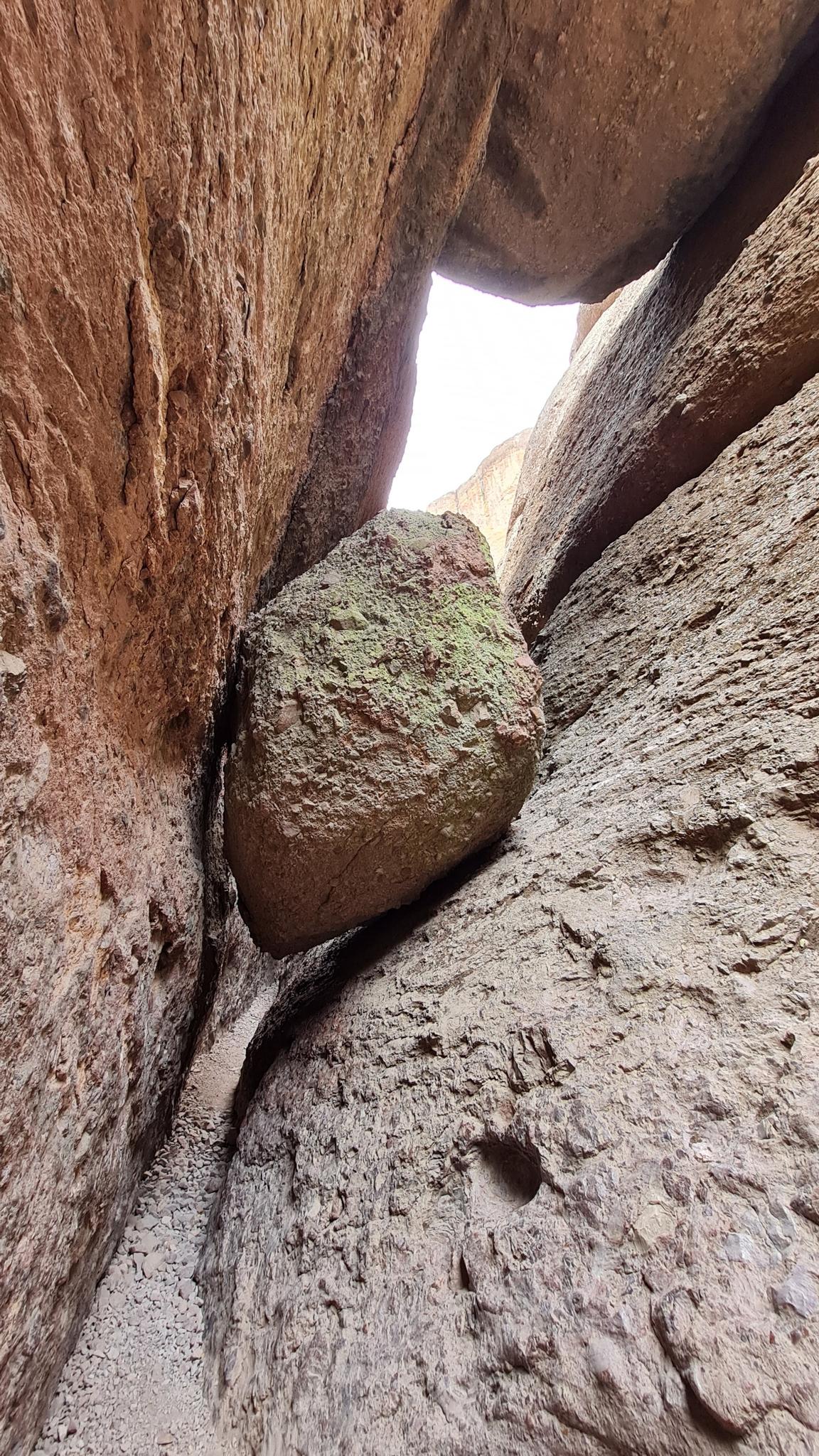 A large boulder wedged tightly between two narrow, rough rock walls.