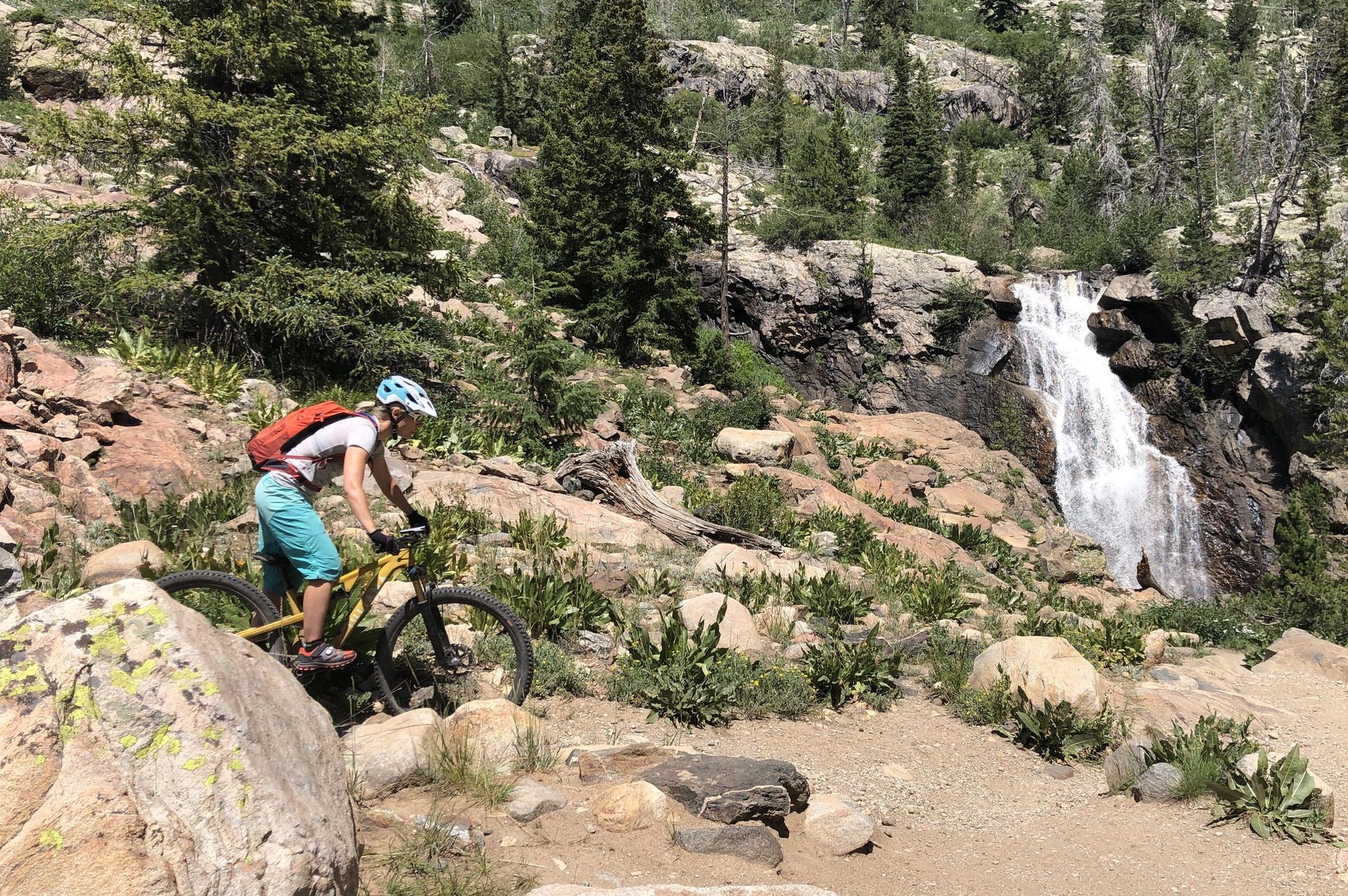 Person on a mountain bike near a waterfall on a sunny day.