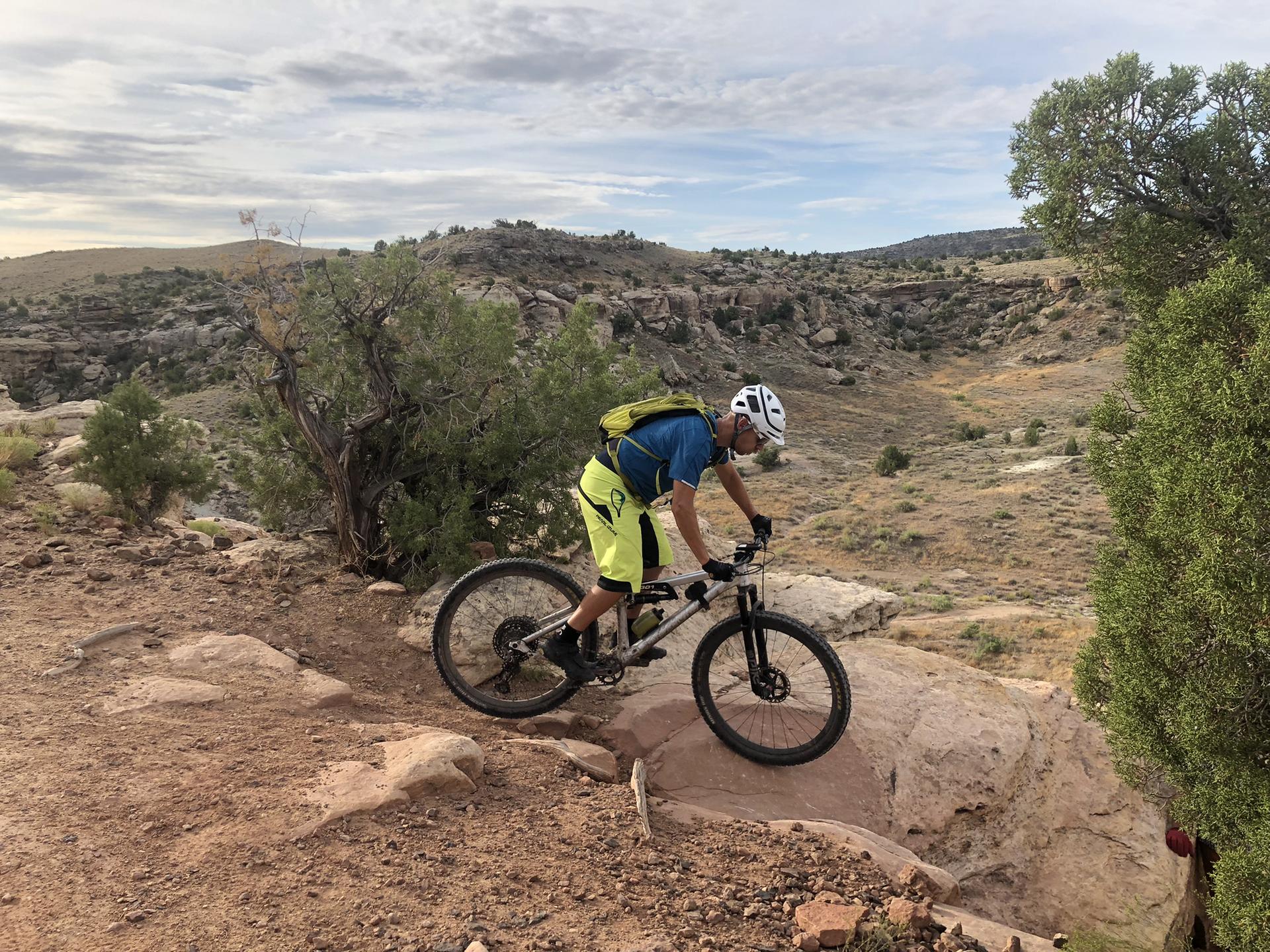 Mountain biker in helmet and bright gear on a rocky desert trail.