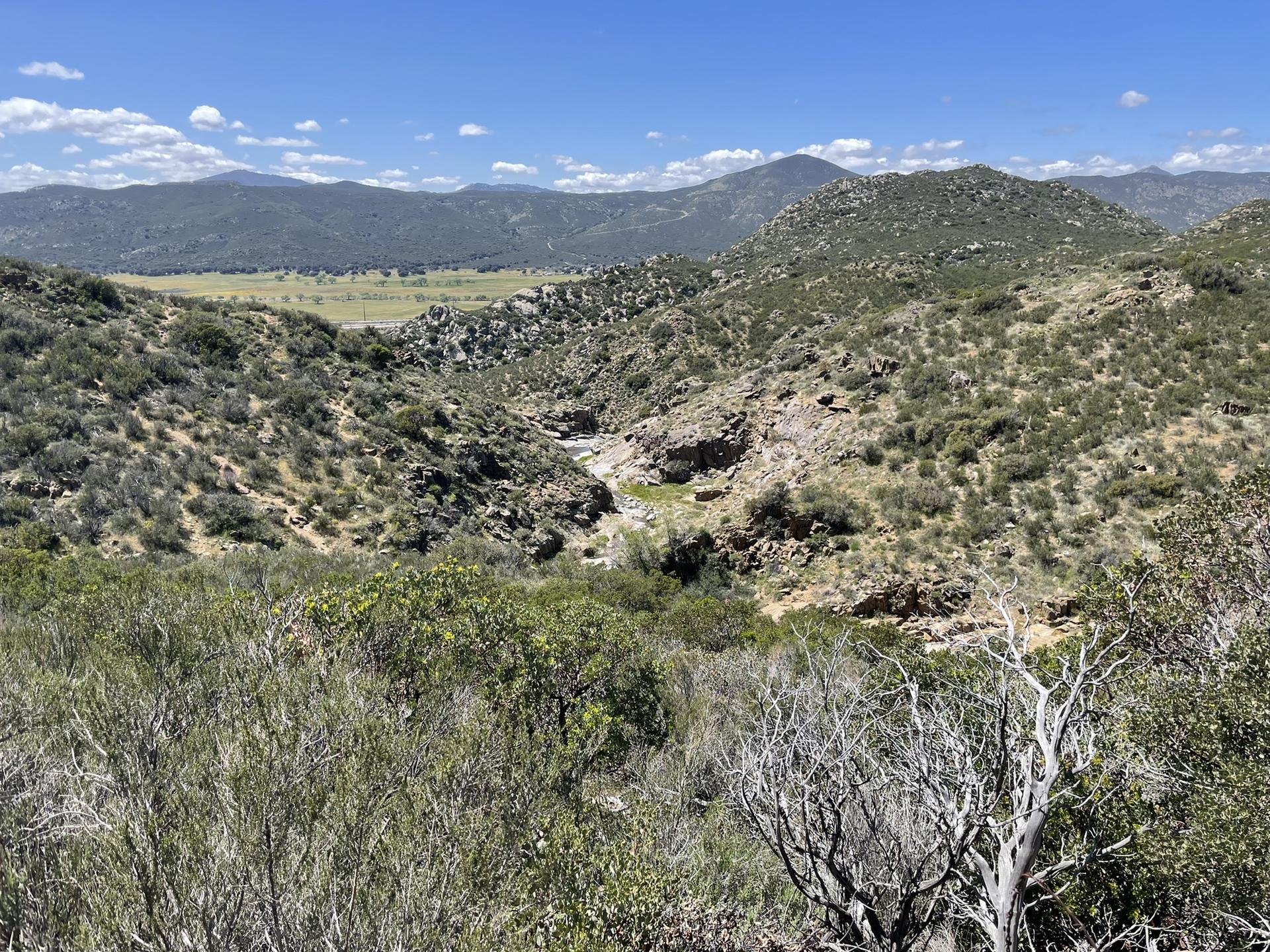 Vast valley with green hills, rocky terrain, and a dry creek bed.
