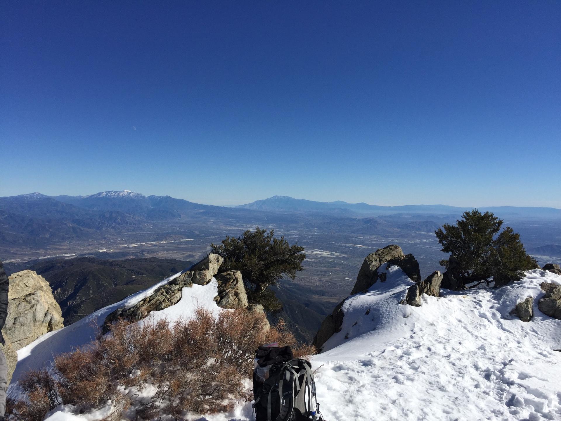 Snowy mountain peak with a backpack, overlooking a vast valley.