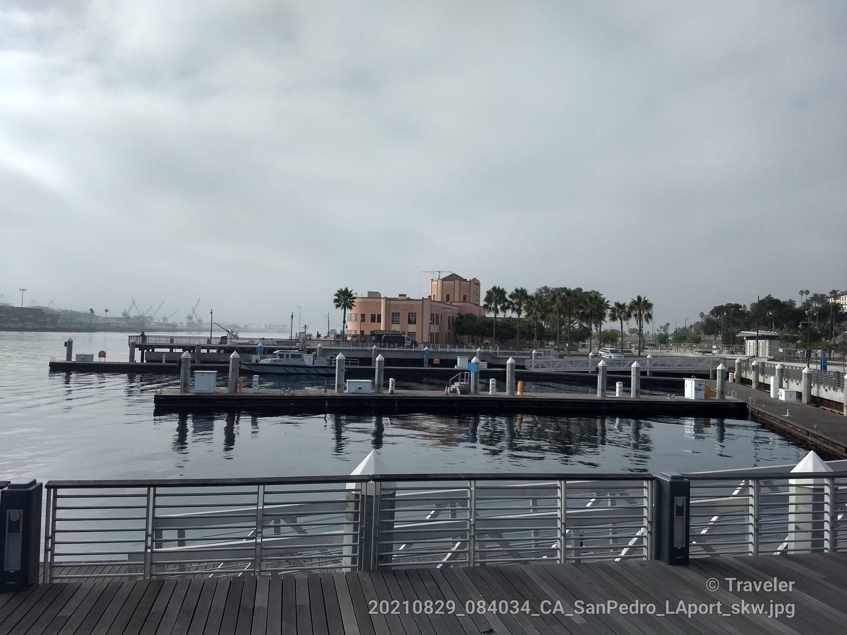 Empty boat docks in calm water with a building under a cloudy sky.