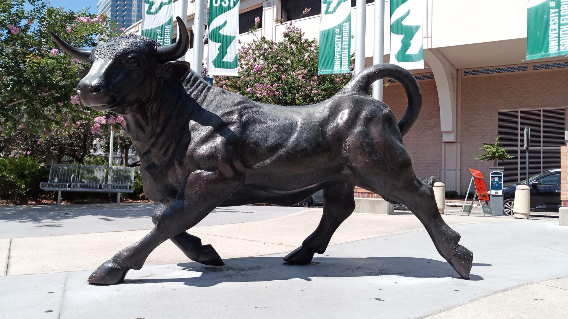 Large bronze bull statue on a sidewalk in front of a building.