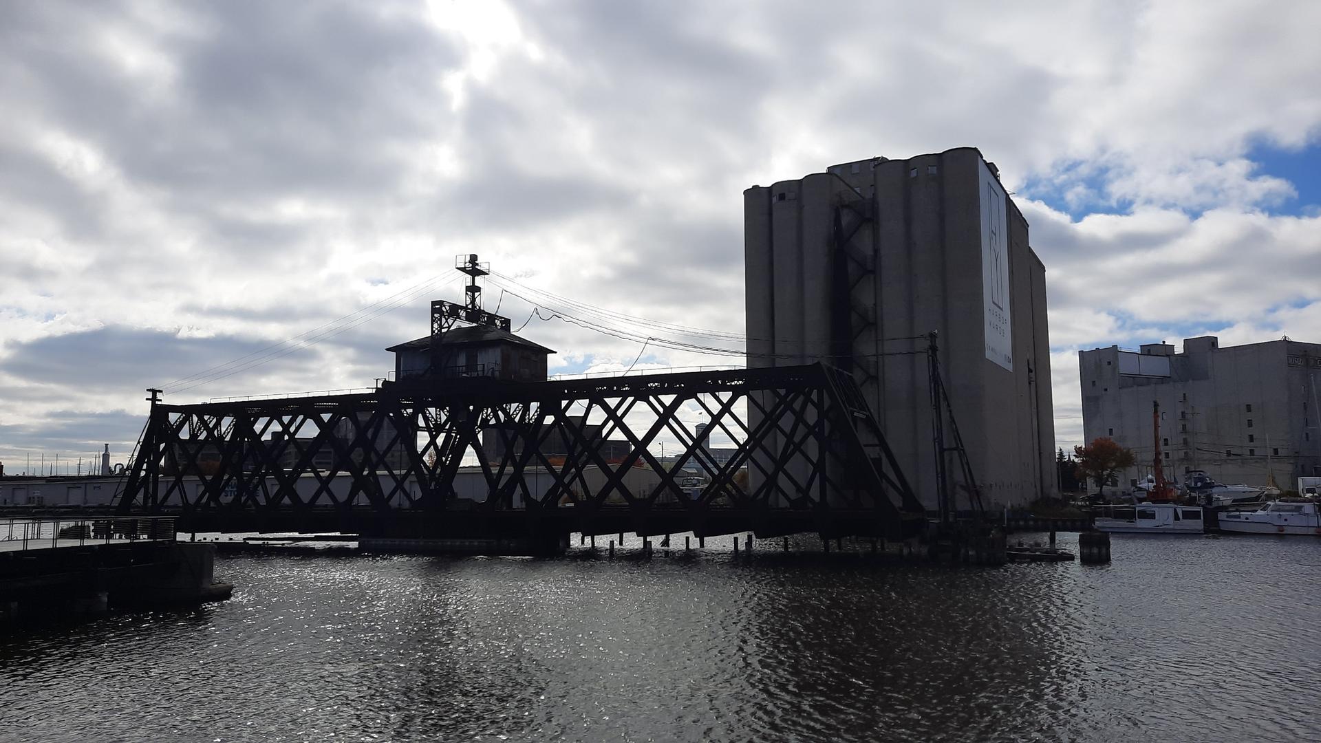An industrial swing bridge over water next to a large concrete building.