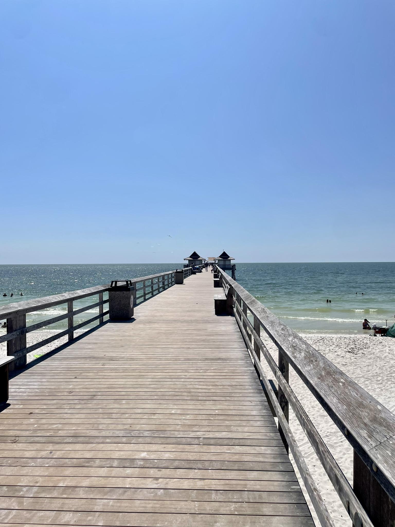 Long wooden pier stretches over the ocean on a clear, sunny day.