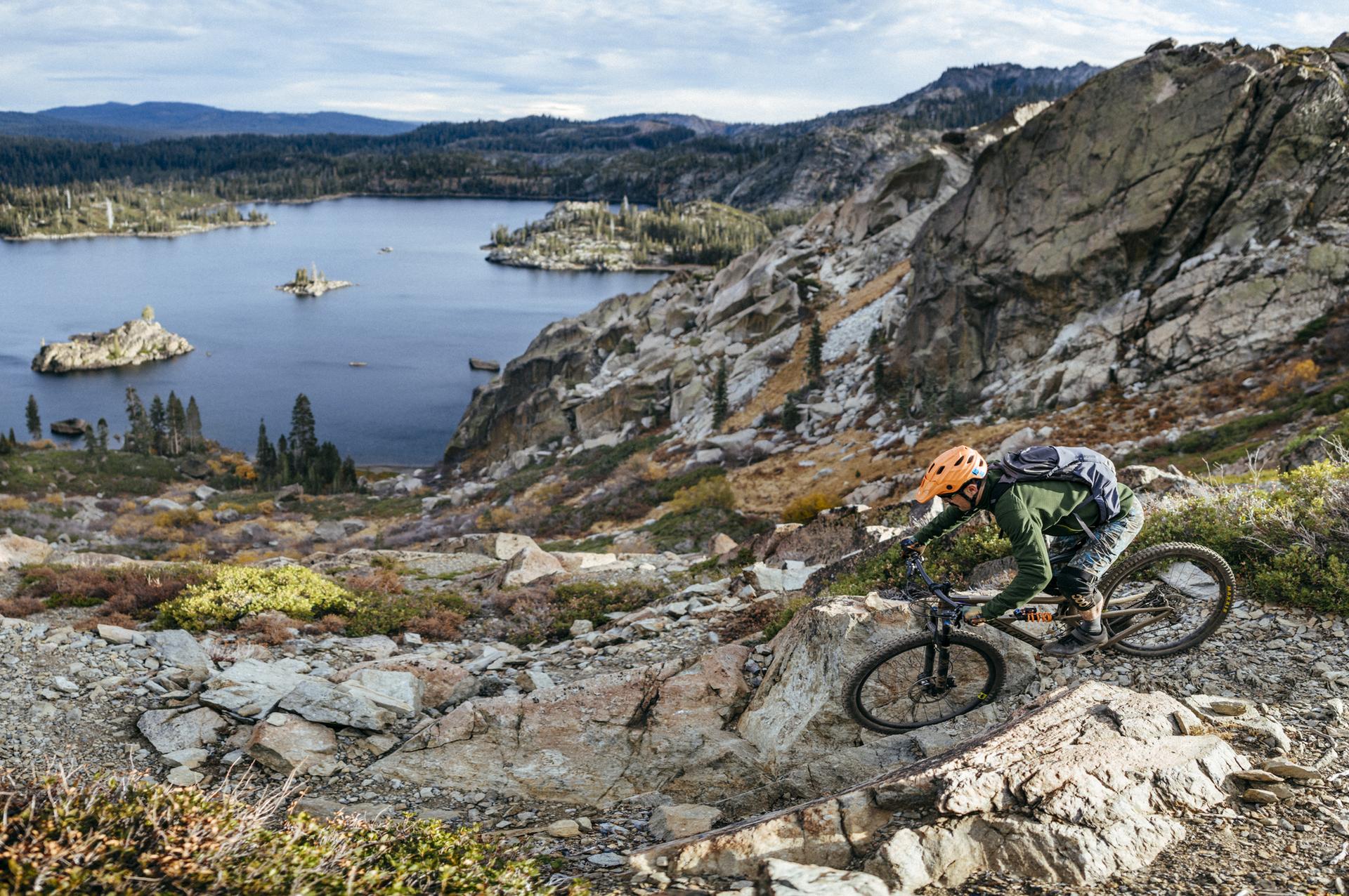 A mountain biker navigates a rocky trail overlooking a large lake.