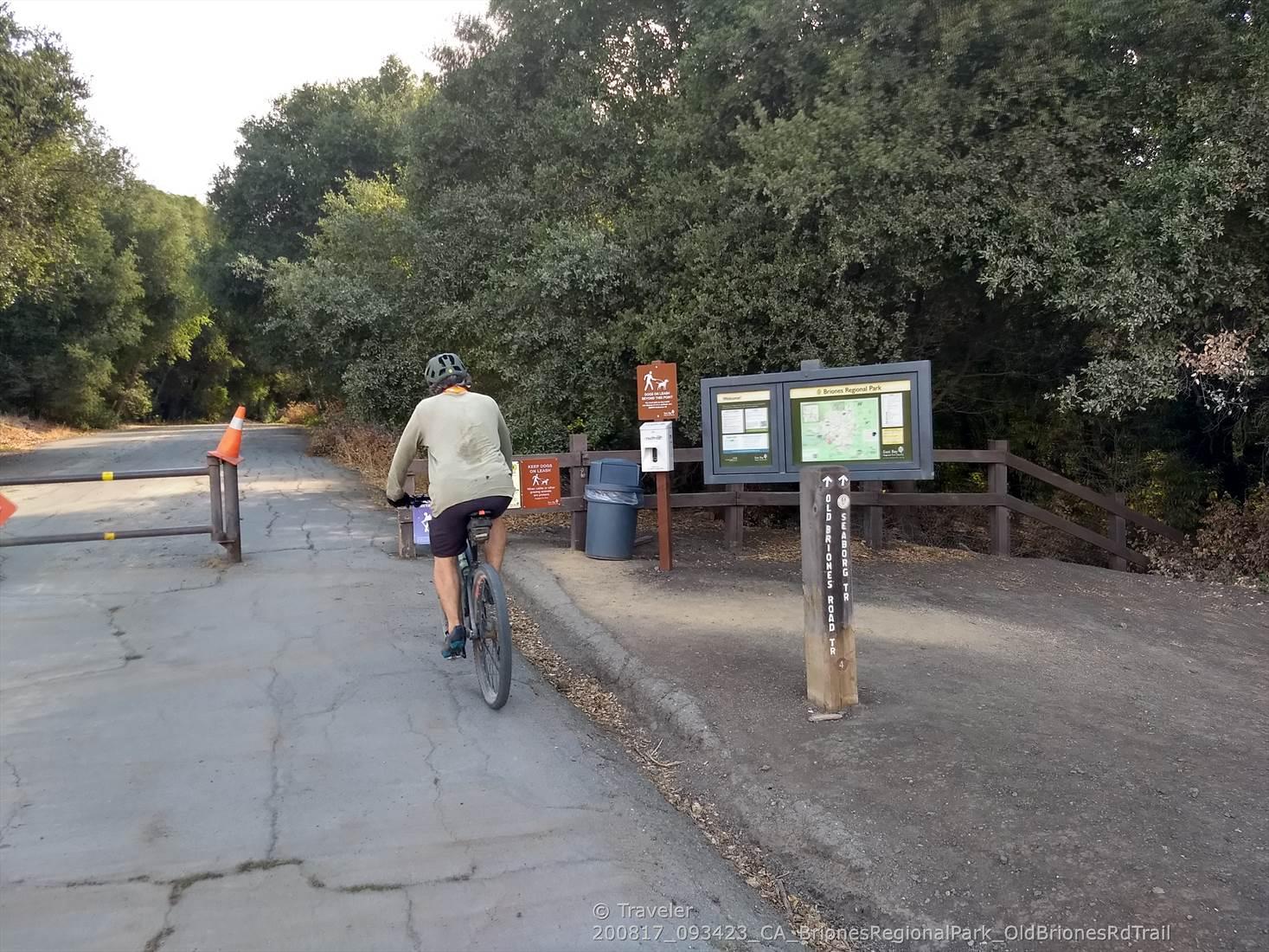 Man on bicycle at a paved trail entrance with an information board.