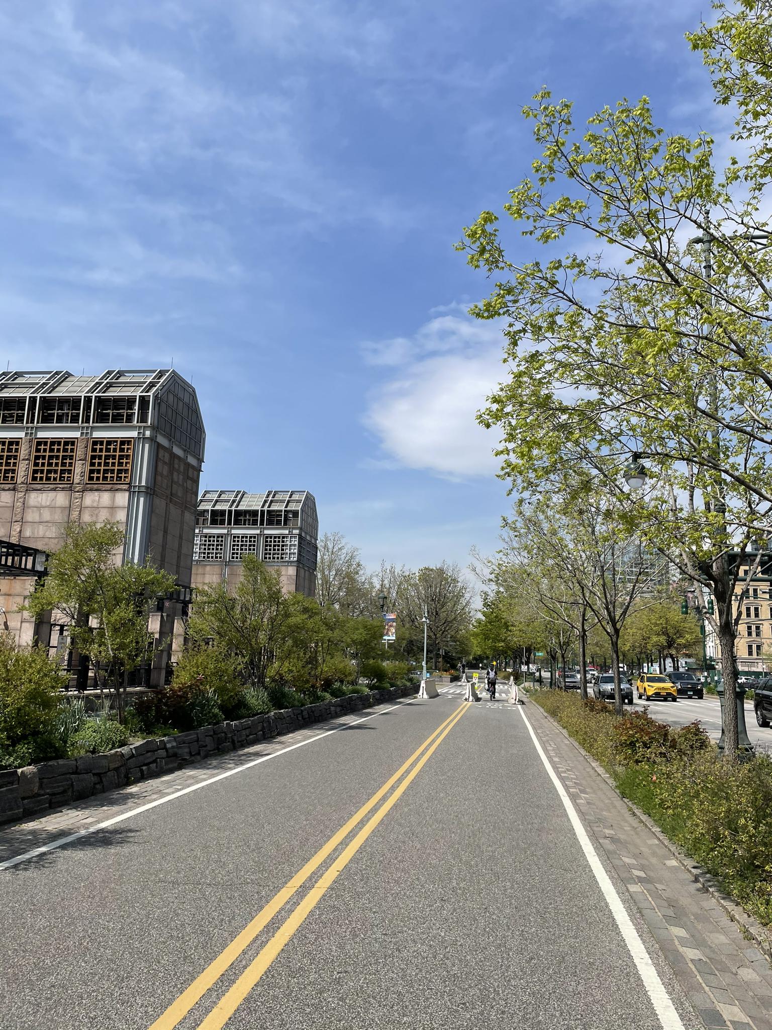 A paved road with buildings and green trees under a bright blue sky.