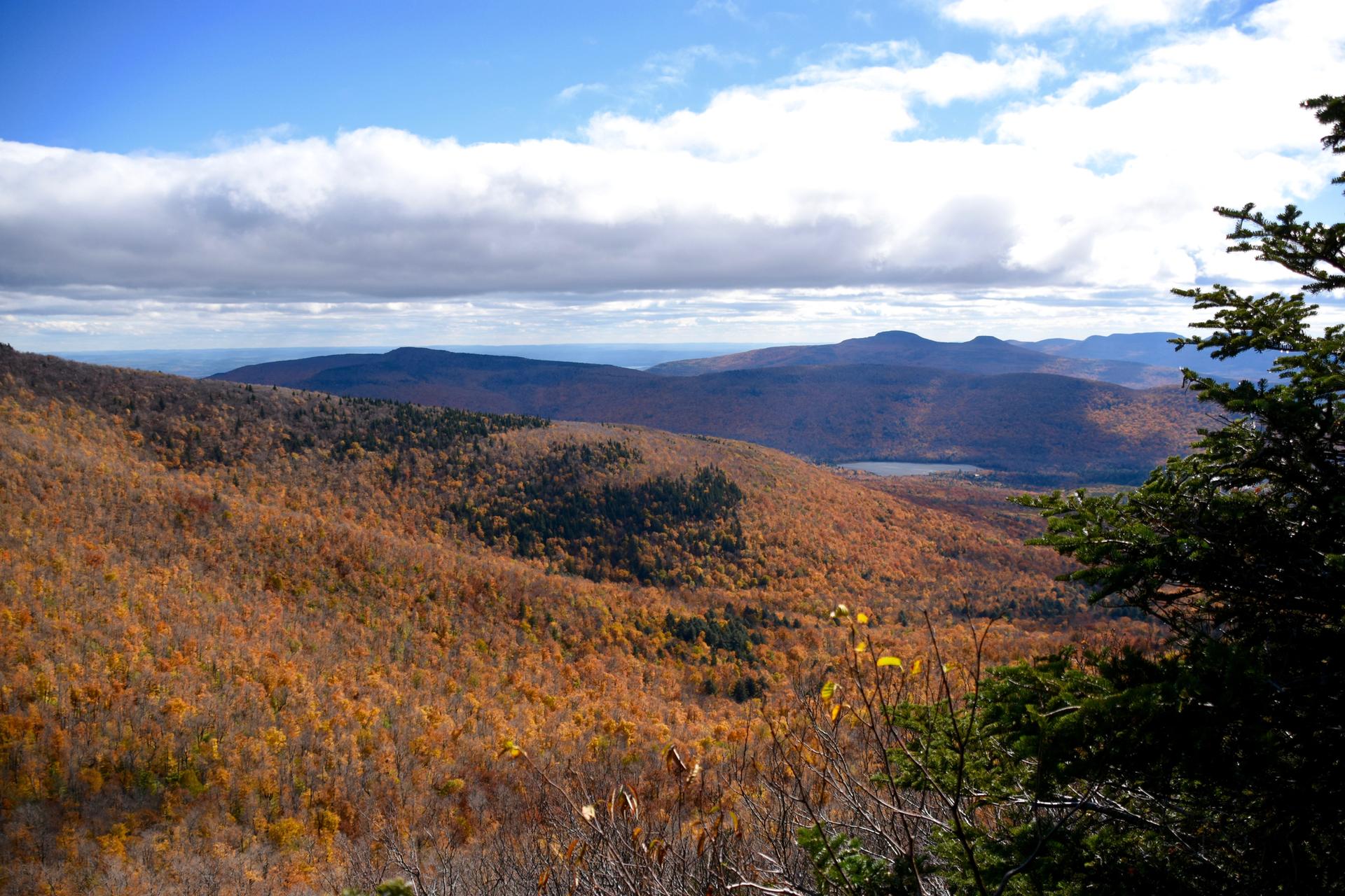 Vast autumn mountain landscape with rolling hills, distant peaks, and a bright sky.