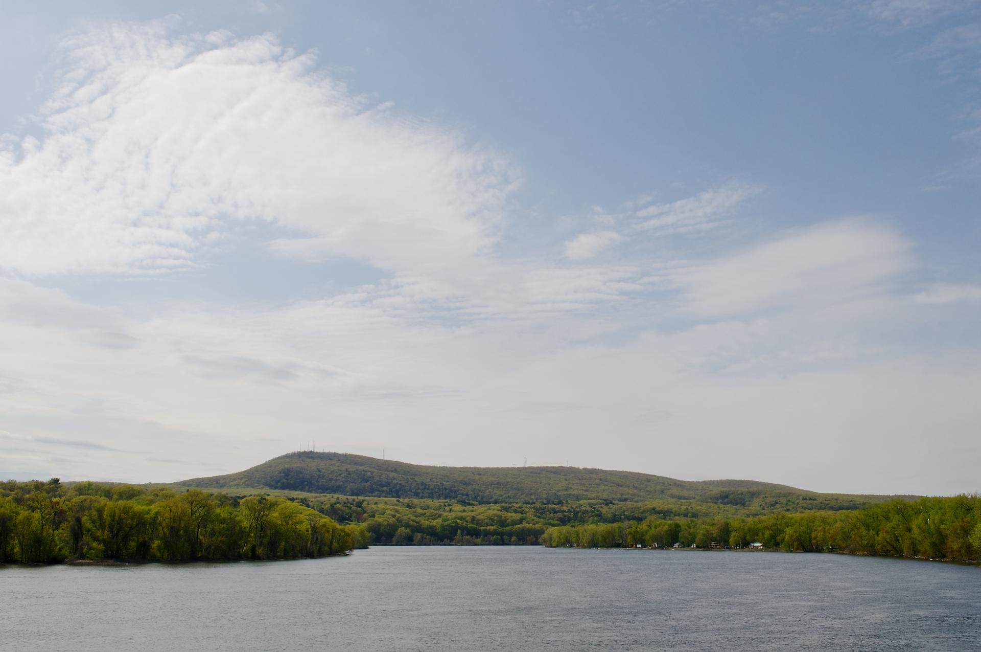 Calm lake surrounded by green forested hills under a partly cloudy sky.
