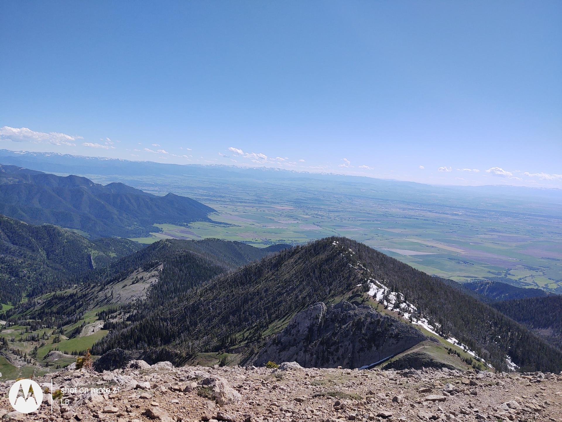 Expansive view from a mountain ridge overlooking forested peaks and distant plains.