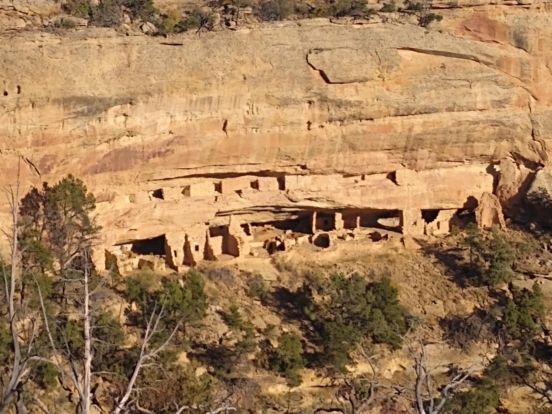 Ancient structures built into a large, sunlit rock cliff face.