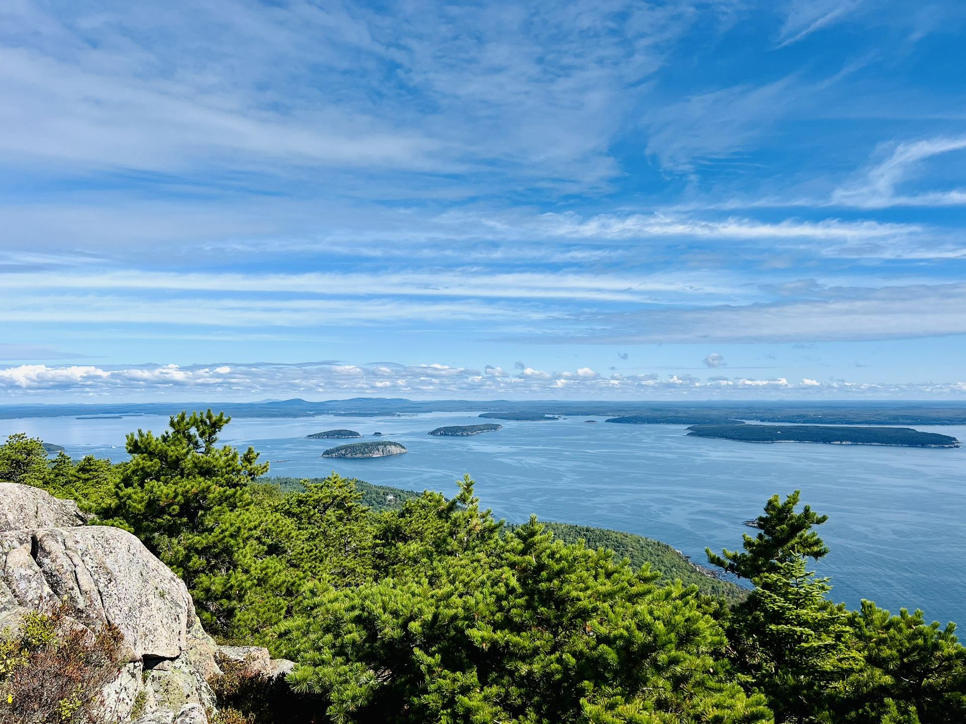 Vast ocean vista from a rocky summit, dotted with numerous green islands.