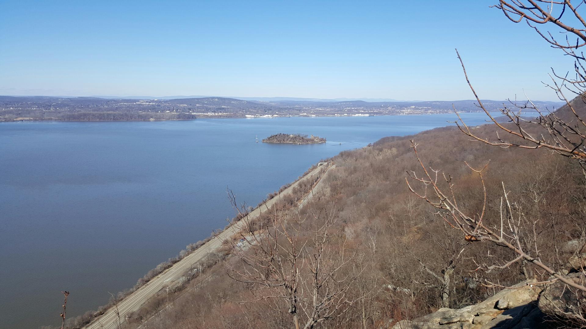 Wide river view with a small island, bare trees on a sunny hillside.