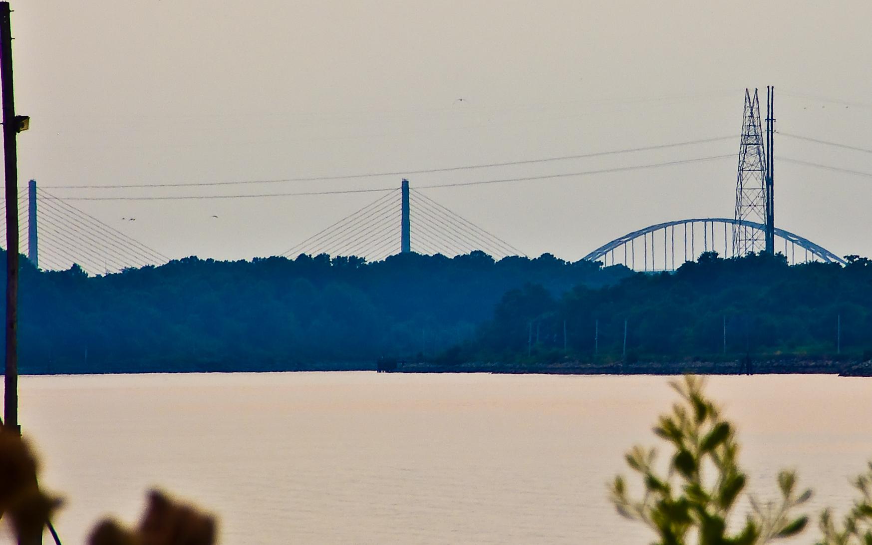 Distant bridges and power lines are visible across a wide river at dusk.