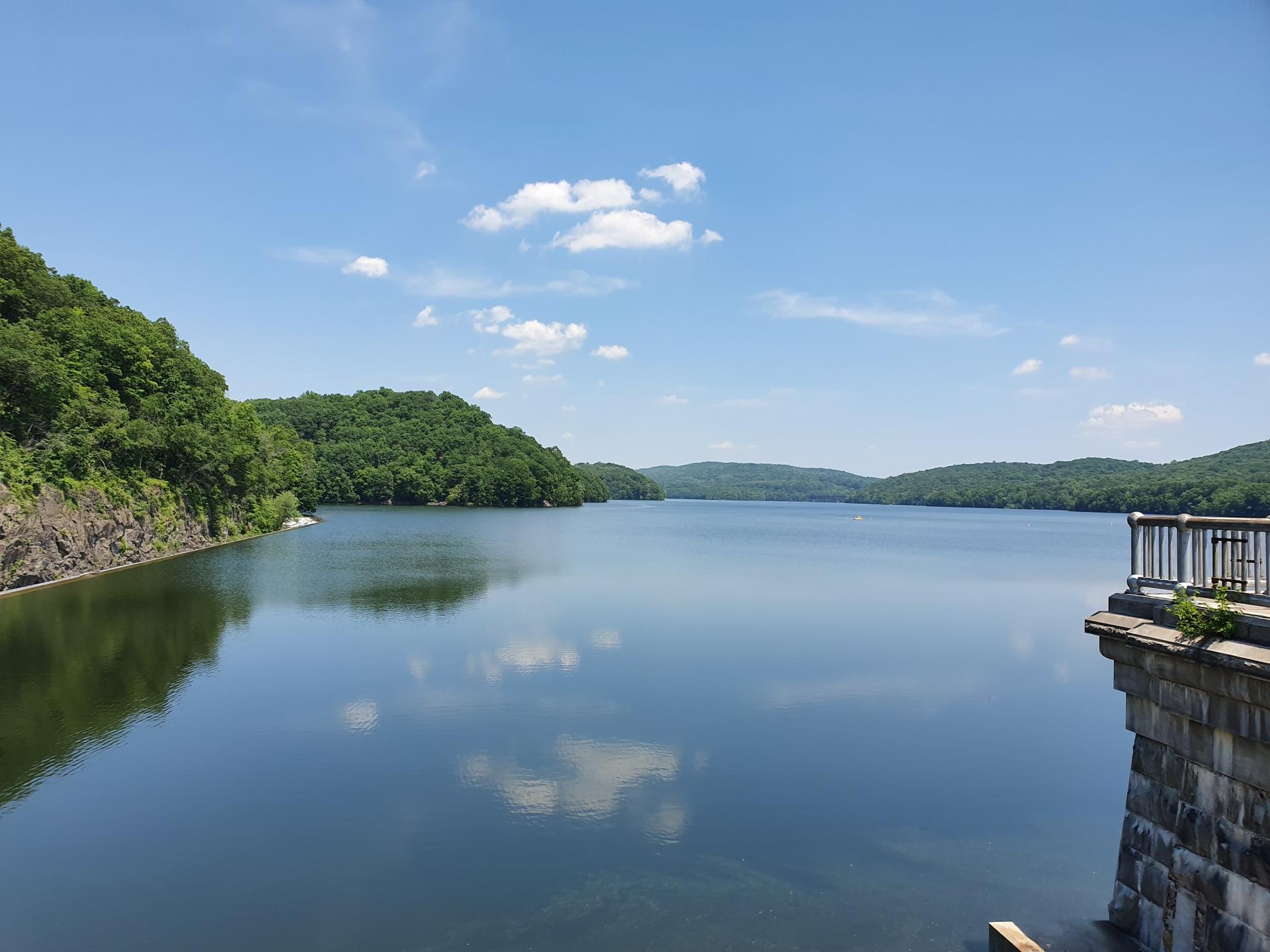 Calm lake reflecting blue sky and clouds, surrounded by green hills.