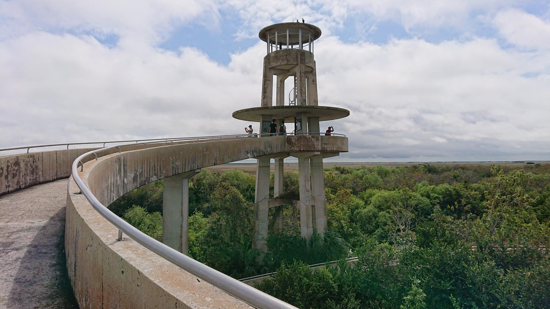 Concrete observation tower with people on a ramp overlooking green landscape.