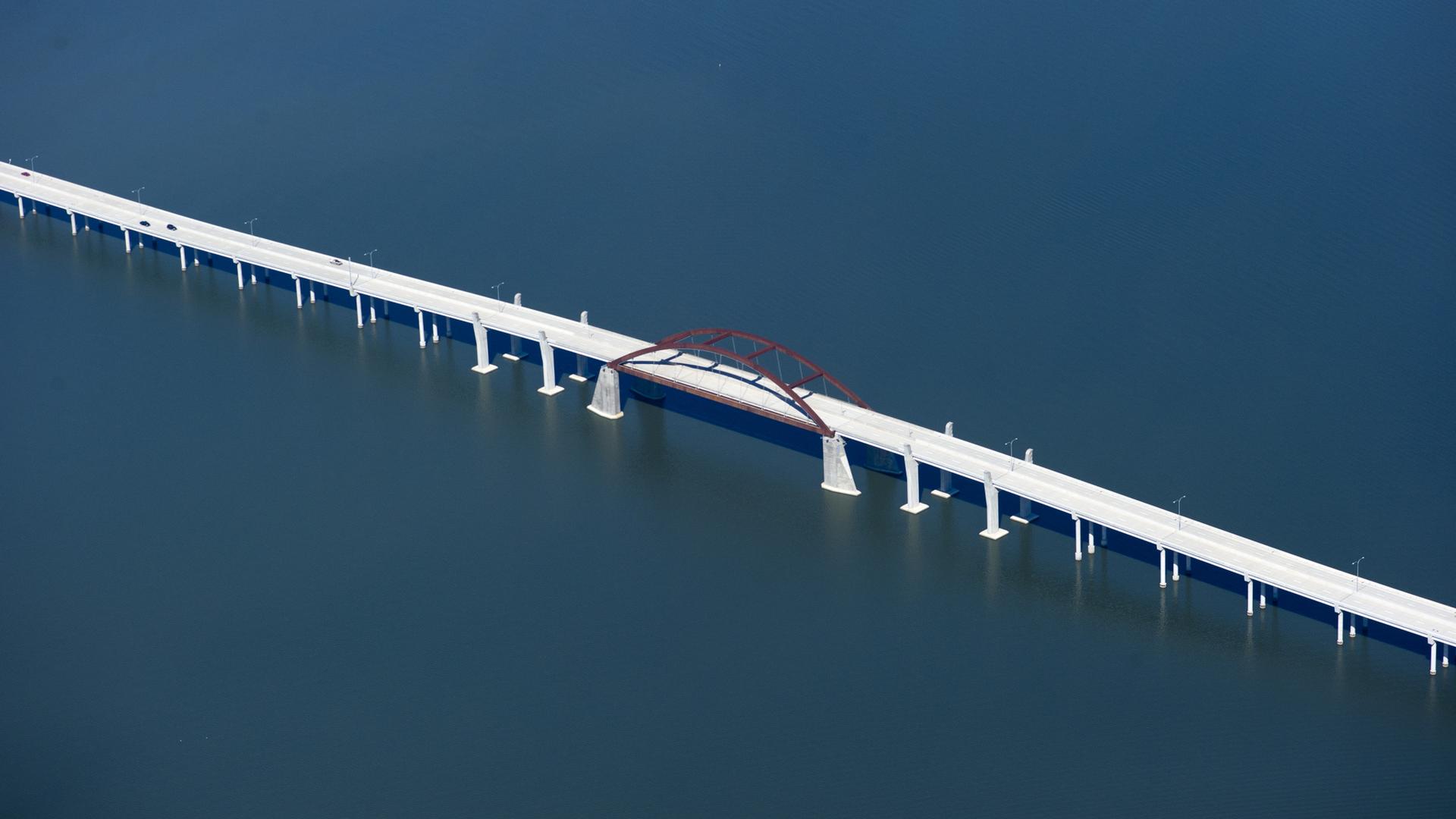 Aerial view of a long white bridge with an arch over dark blue water.