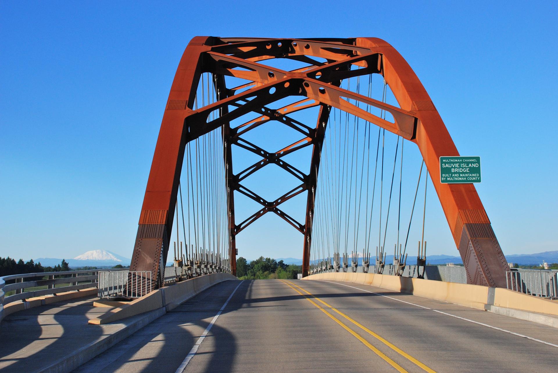 Large orange arch bridge over a road on a clear, sunny day.