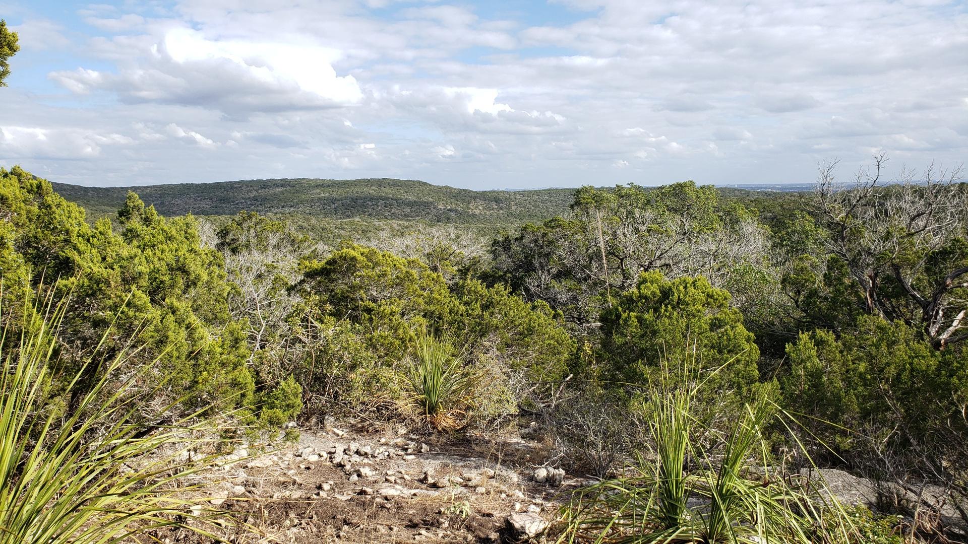 Overlook of a vast, hilly, green landscape with a cloudy sky.