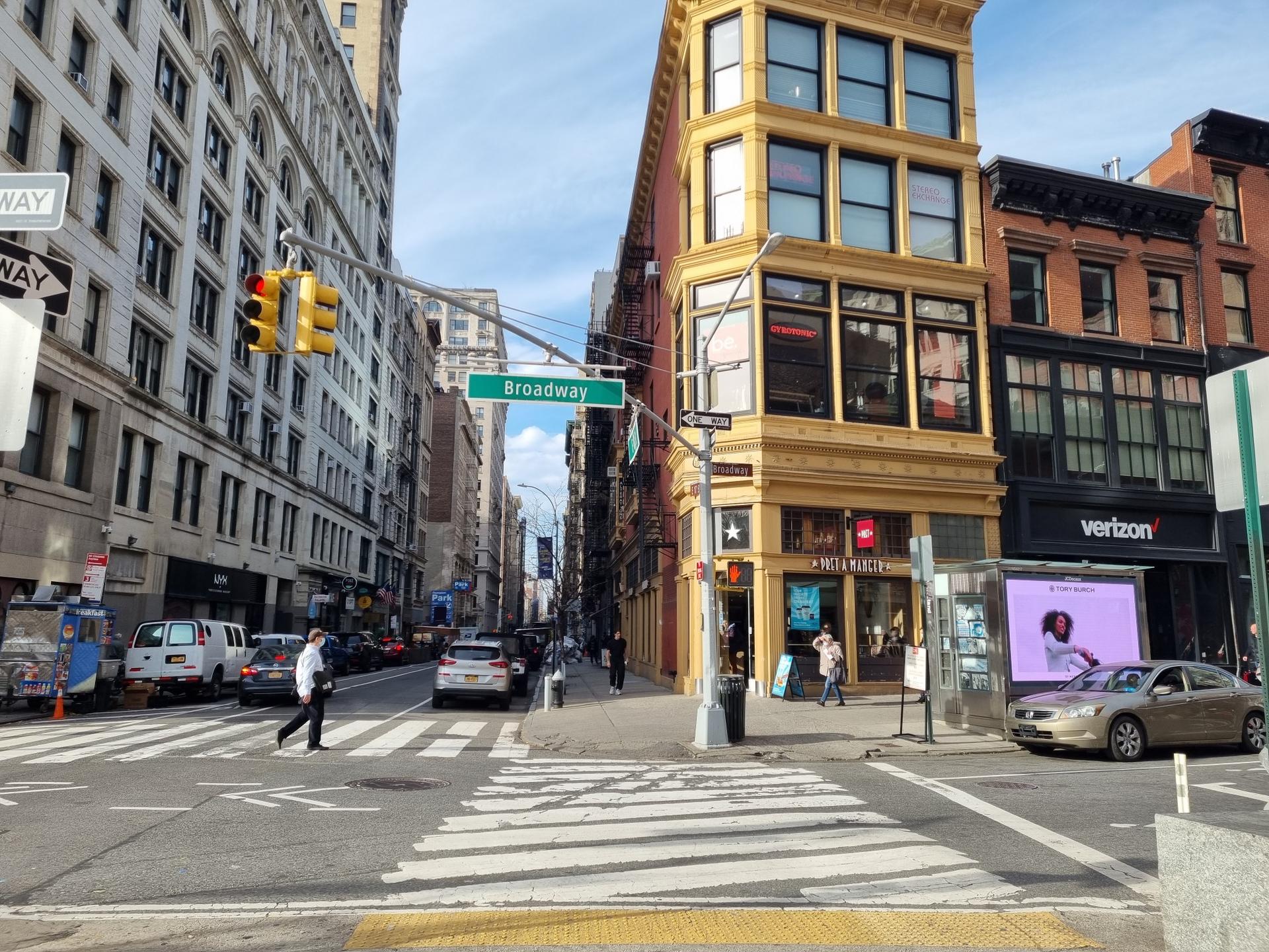 Busy city intersection with a yellow building, cars, and pedestrians.