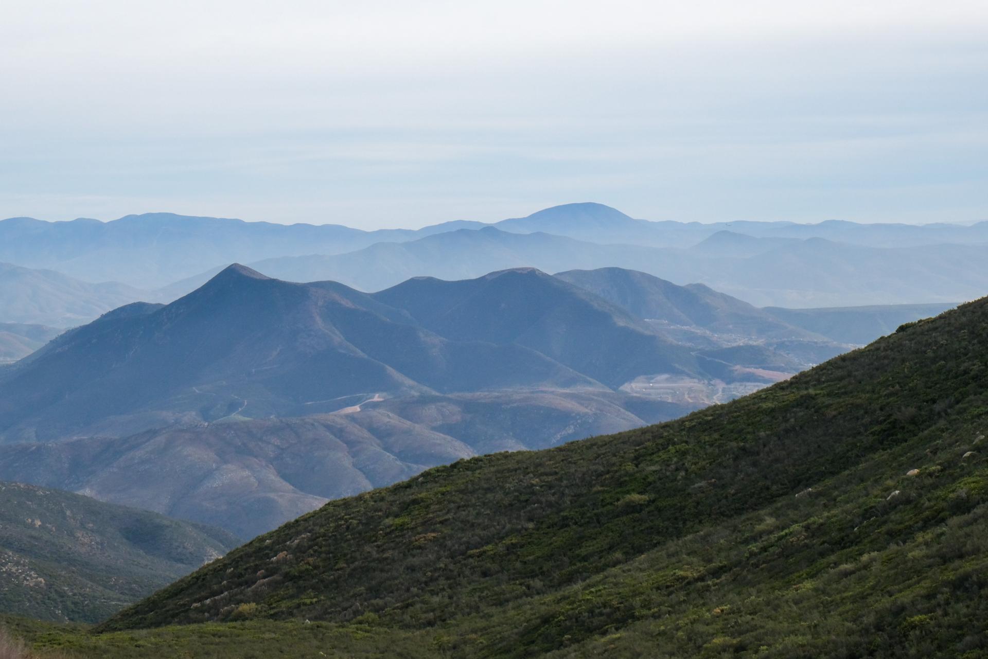 Distant hazy mountains and a steep, brush-covered slope under a soft sky.