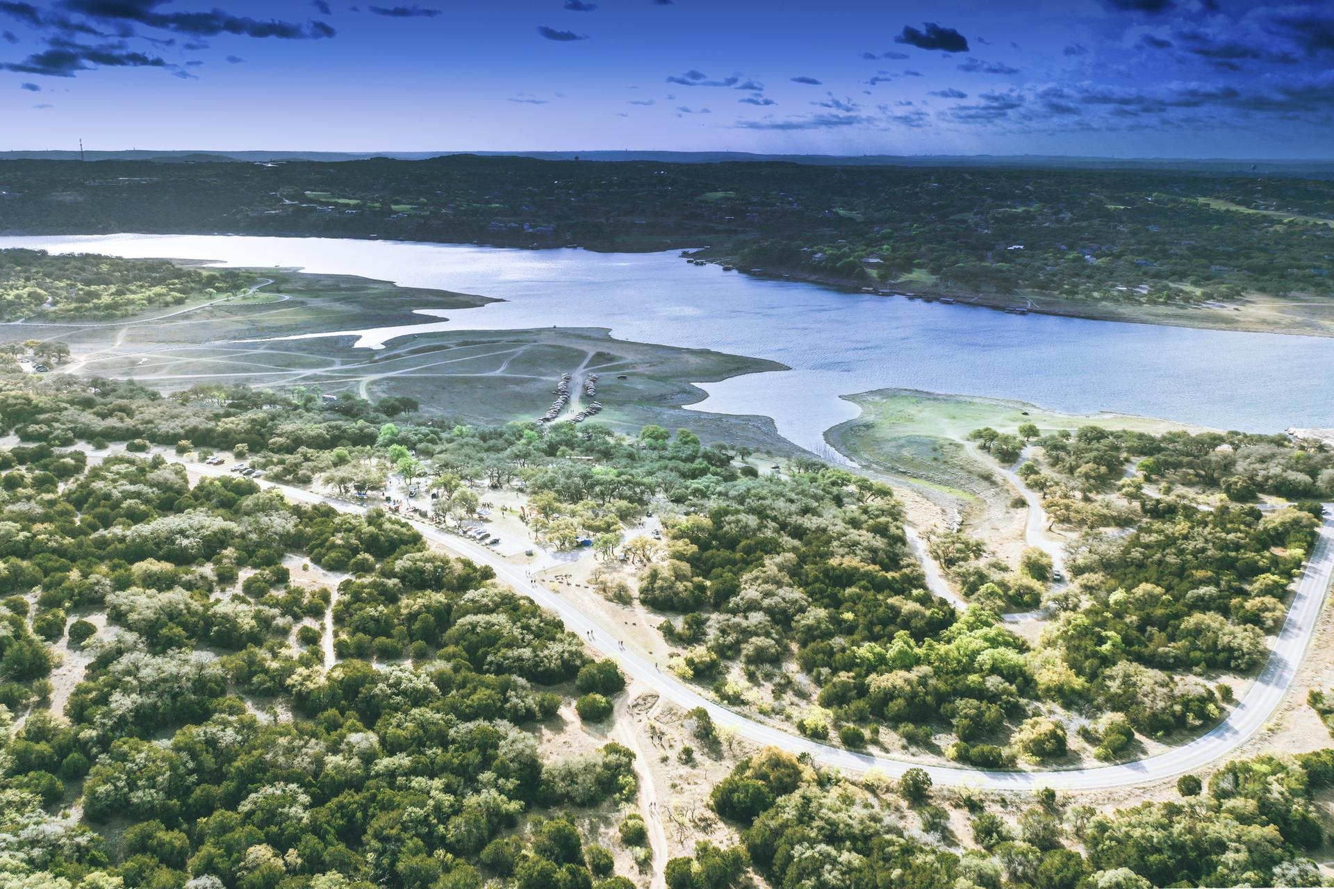 Expansive aerial view of a lake, dense green foliage, and winding roads.