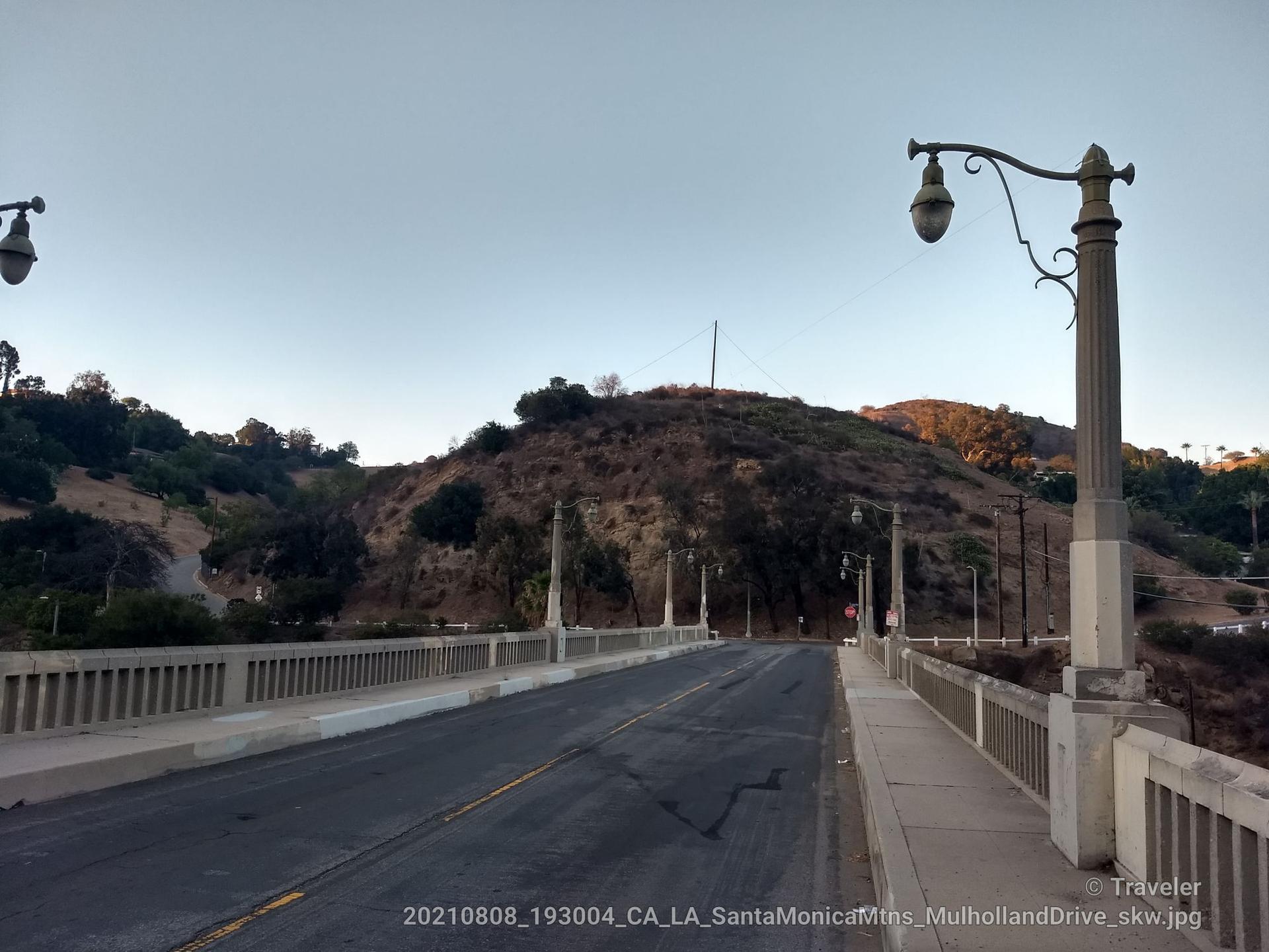 An empty concrete bridge with ornate streetlights leading to dry hills.
