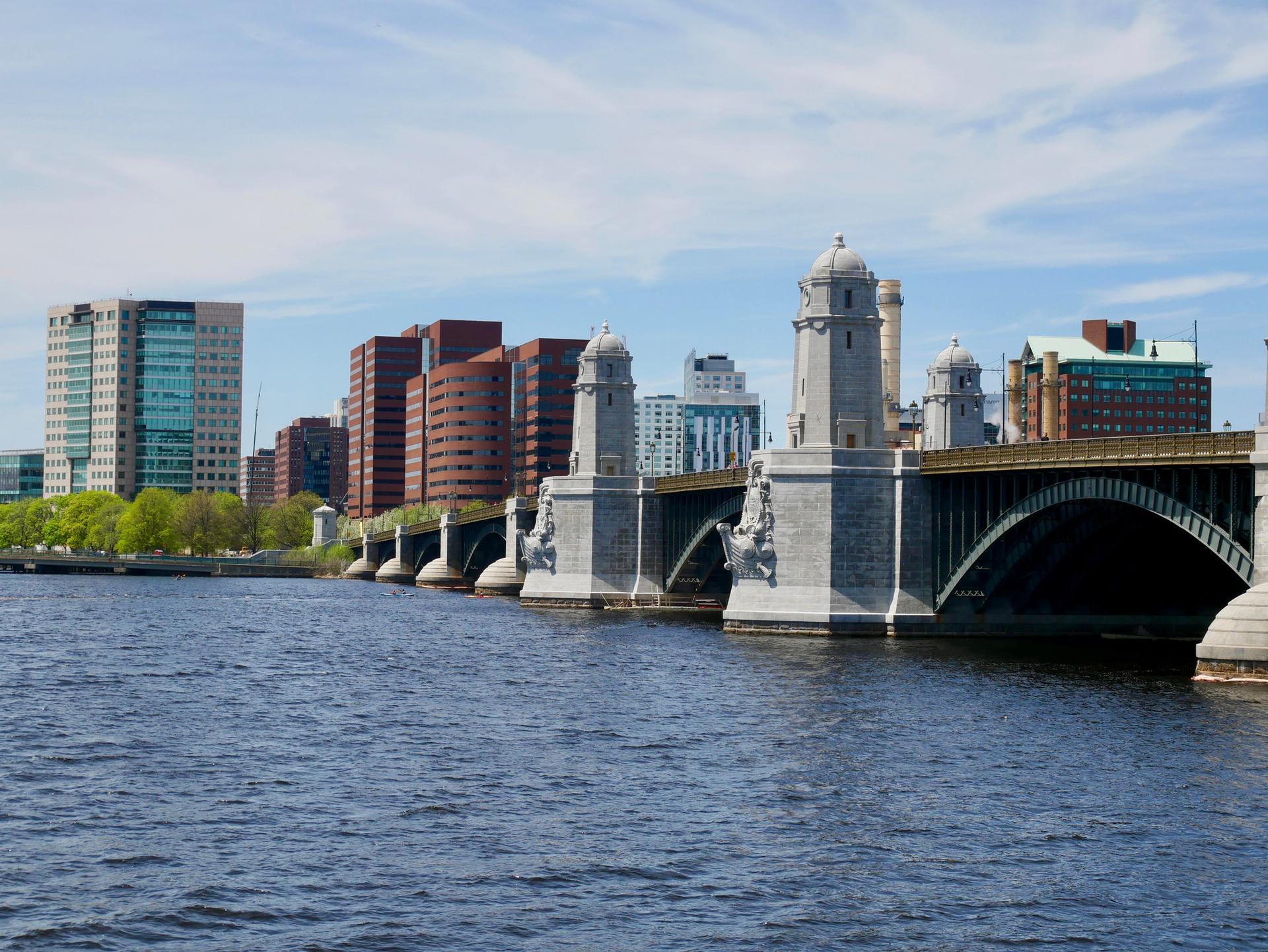 Large stone bridge with towers over a river, city skyline under bright sky.