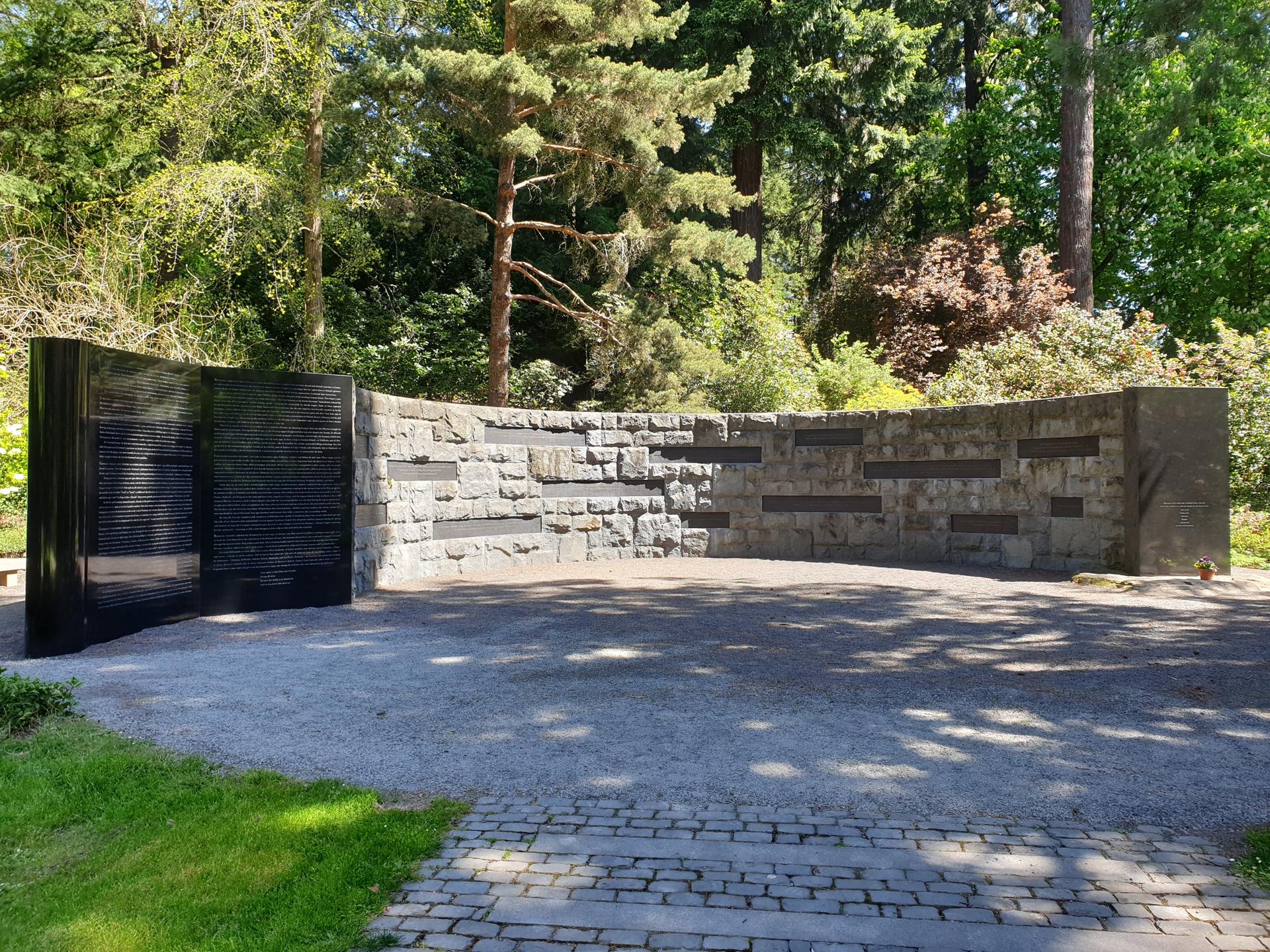 A curved stone and black wall monument in a sunny park setting.