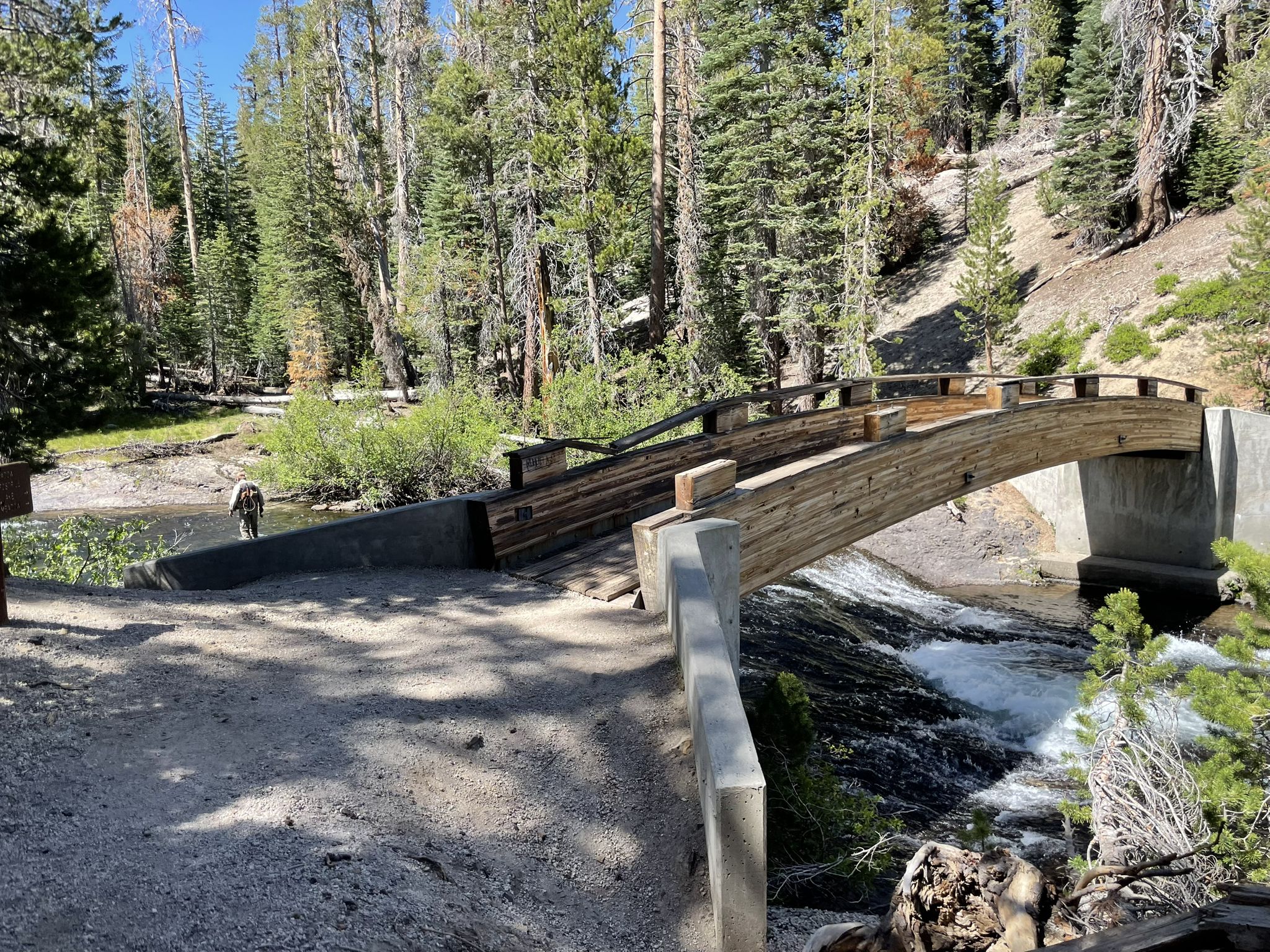 Arched wooden bridge over a flowing river, with a person and pine trees. - San Joaquin River via the Pacific Crest Trail