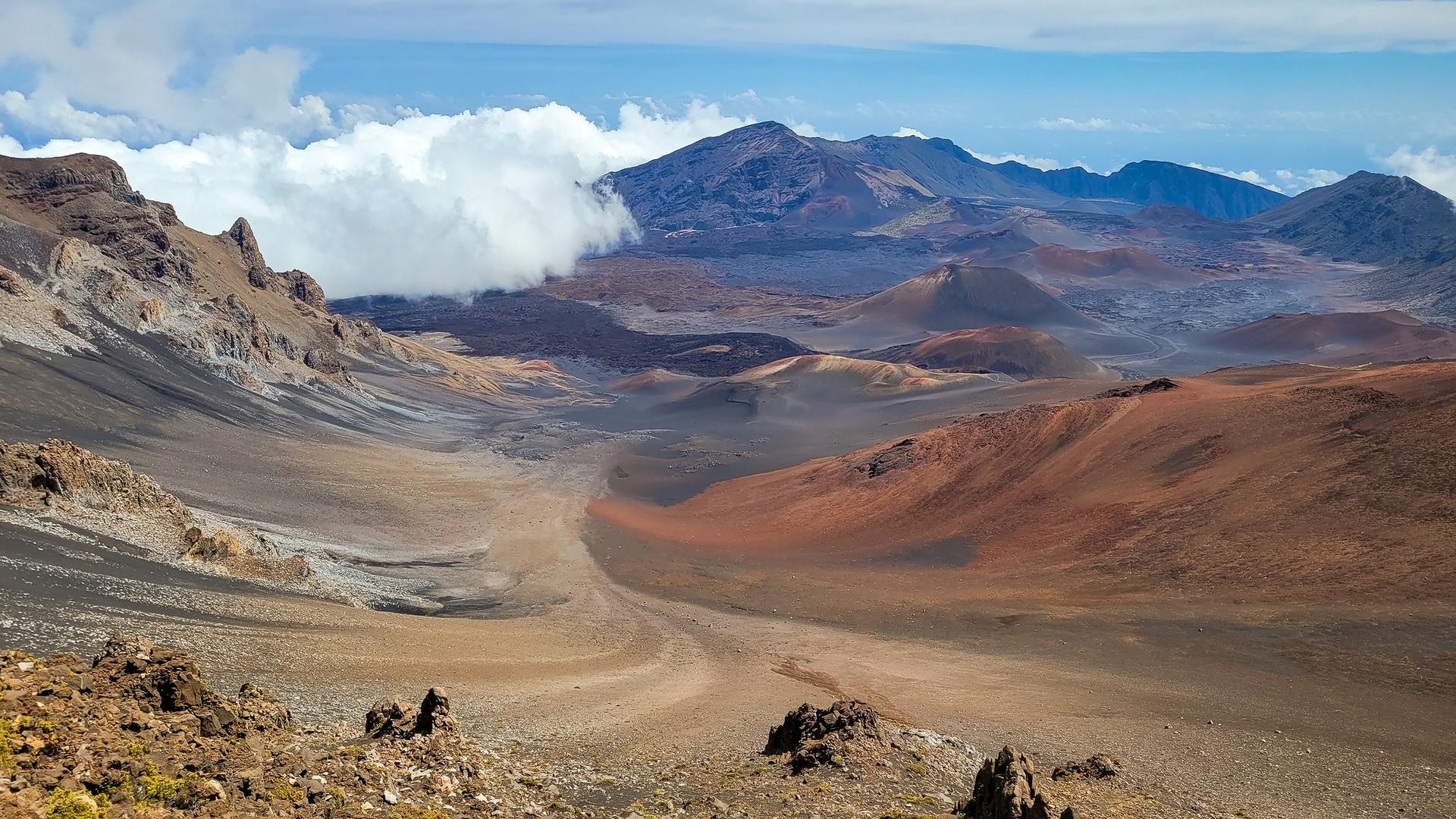 Panoramic view of a vast volcanic valley with colorful slopes and distant clouds.