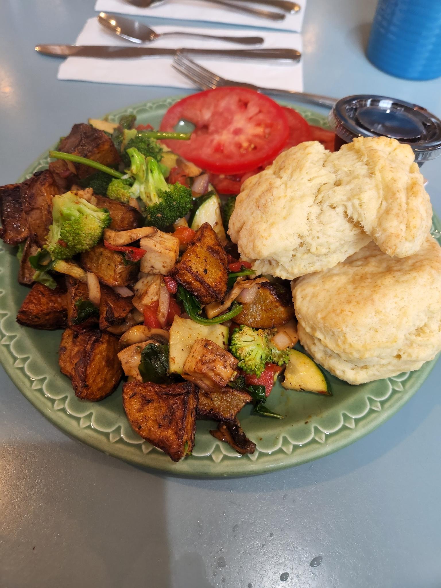A plate of breakfast food with biscuits, fried potatoes, broccoli, and sliced tomatoes.