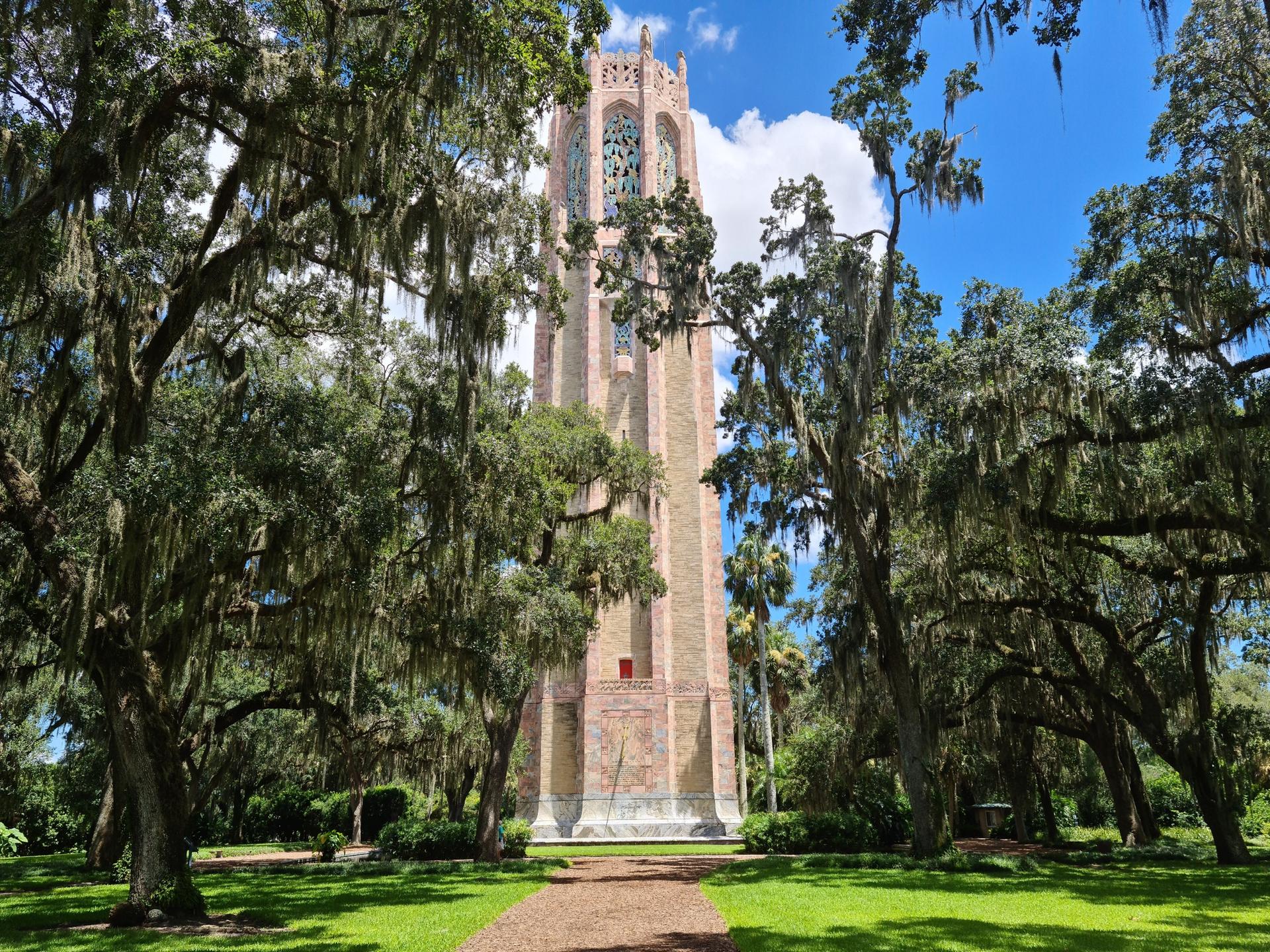 Tall, ornate tower framed by moss-draped trees on a sunny day.