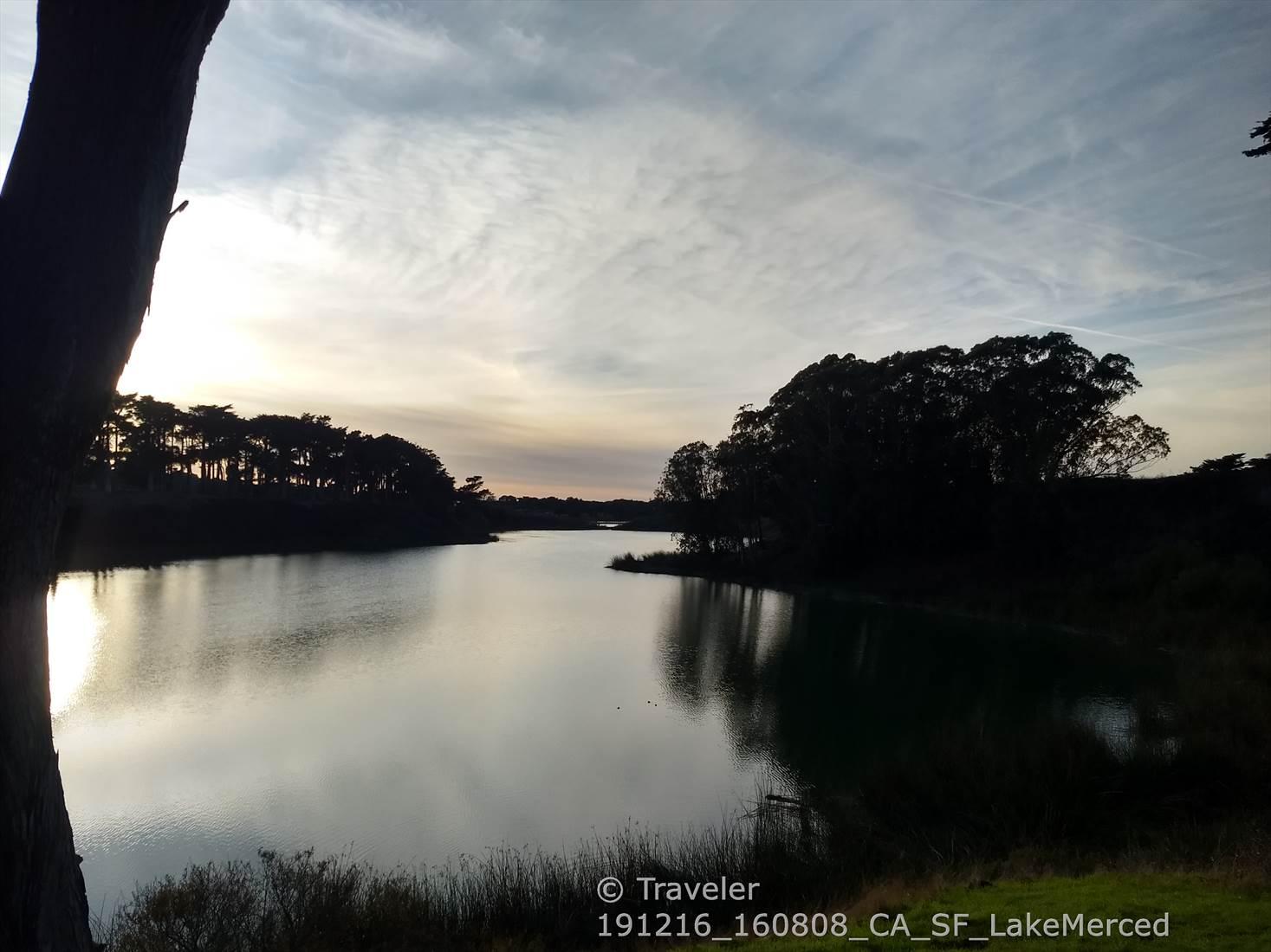 A serene lake at dusk, reflecting the colorful sky, framed by dark trees.