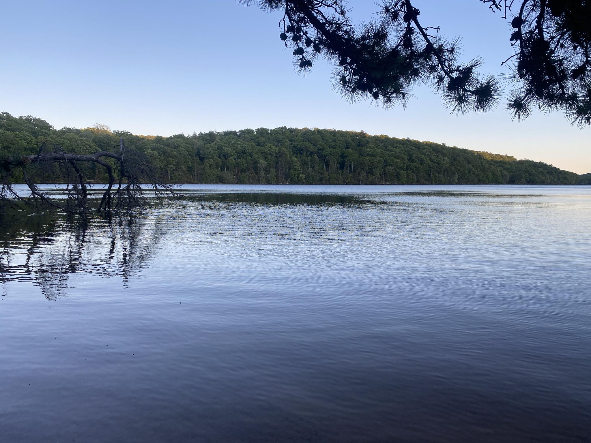Calm lake reflecting forested hills under a clear evening sky.