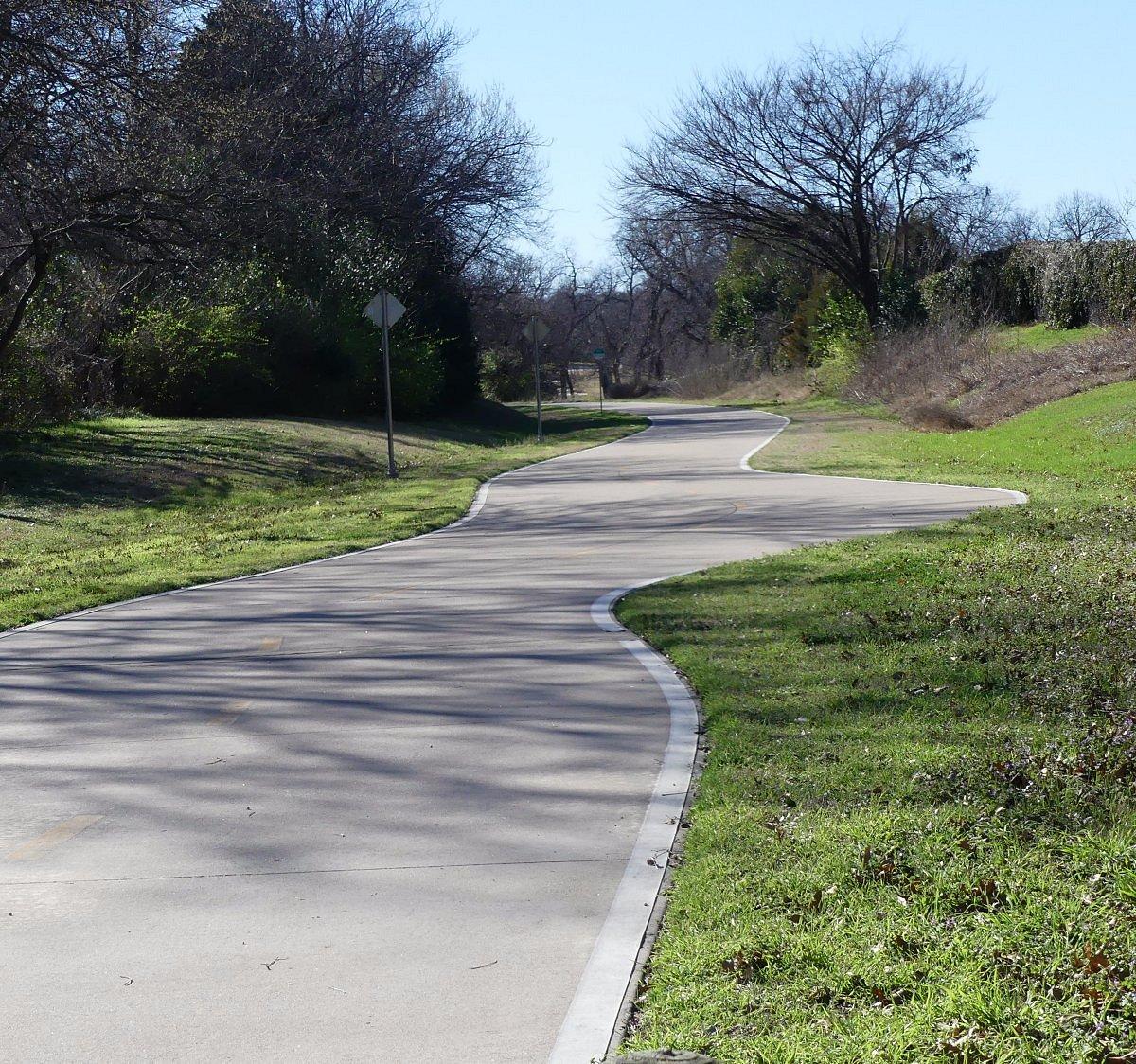 A winding paved path through a grassy landscape with bare trees.
