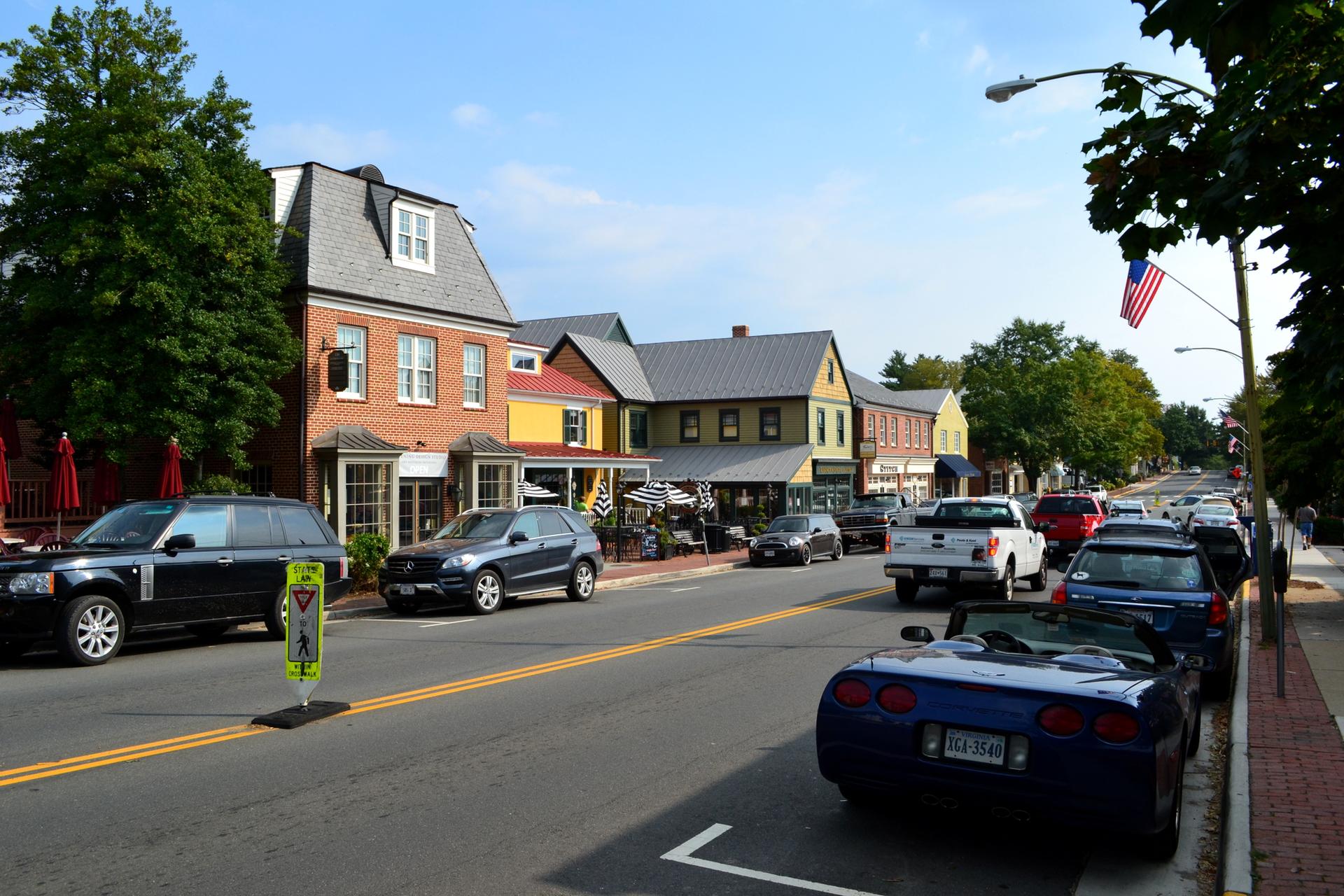 A sunny street scene with parked cars, brick buildings, and an American flag.