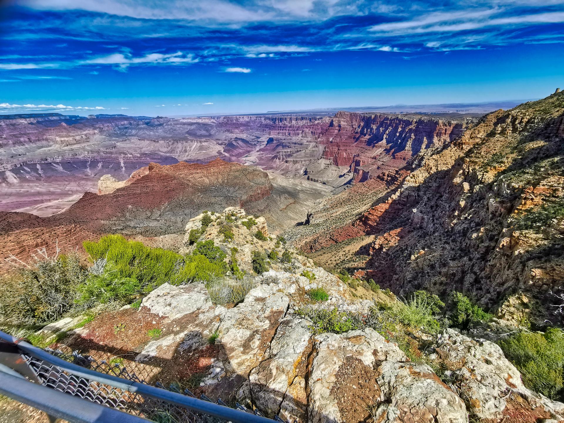 Expansive, colorful canyon landscape under a bright blue sky with white clouds.