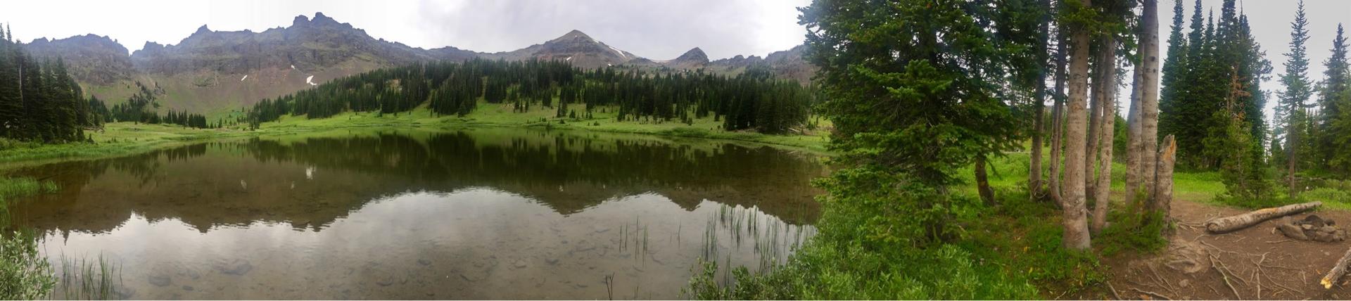Overcast panoramic view of a mountain lake reflecting rocky peaks and trees.