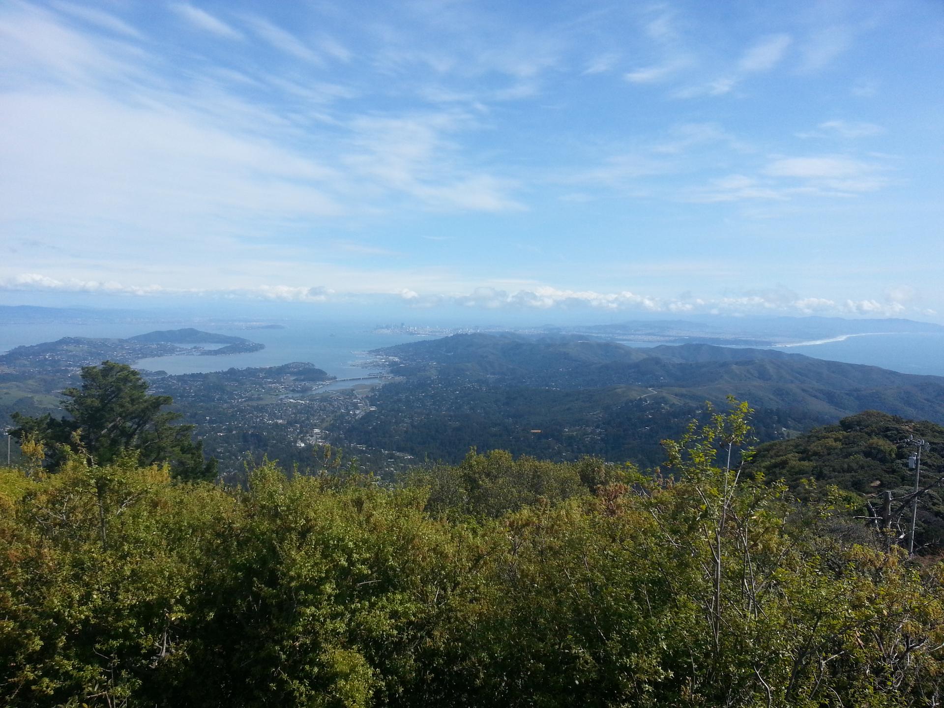 Expansive view of a bay and green hills under a bright sky.