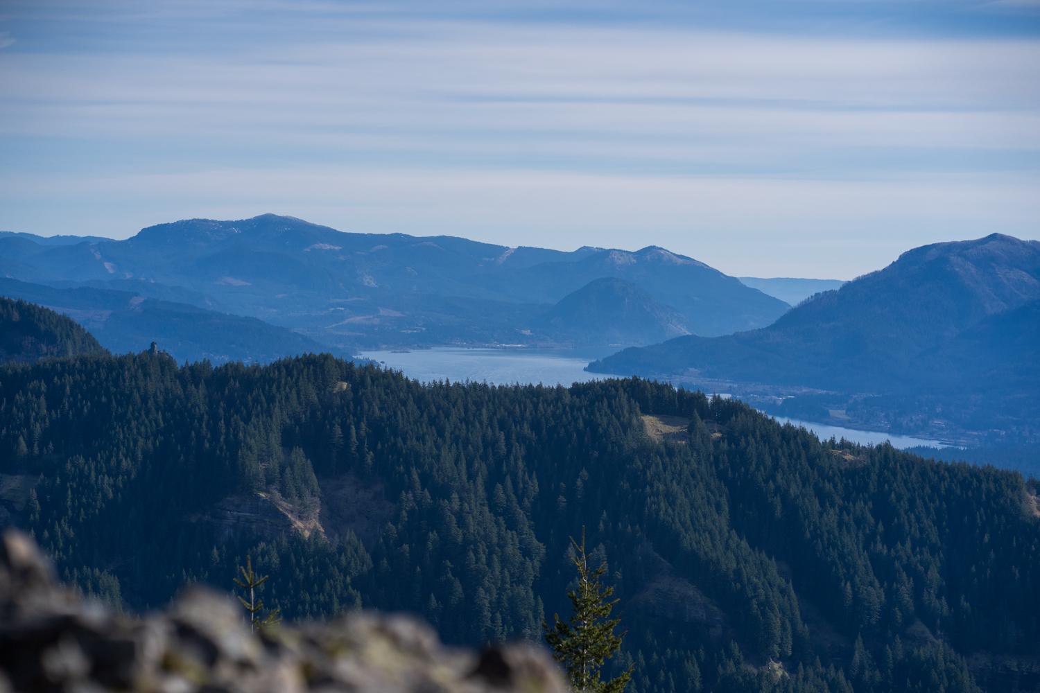 Distant lake nestled between forested mountains under a hazy sky.