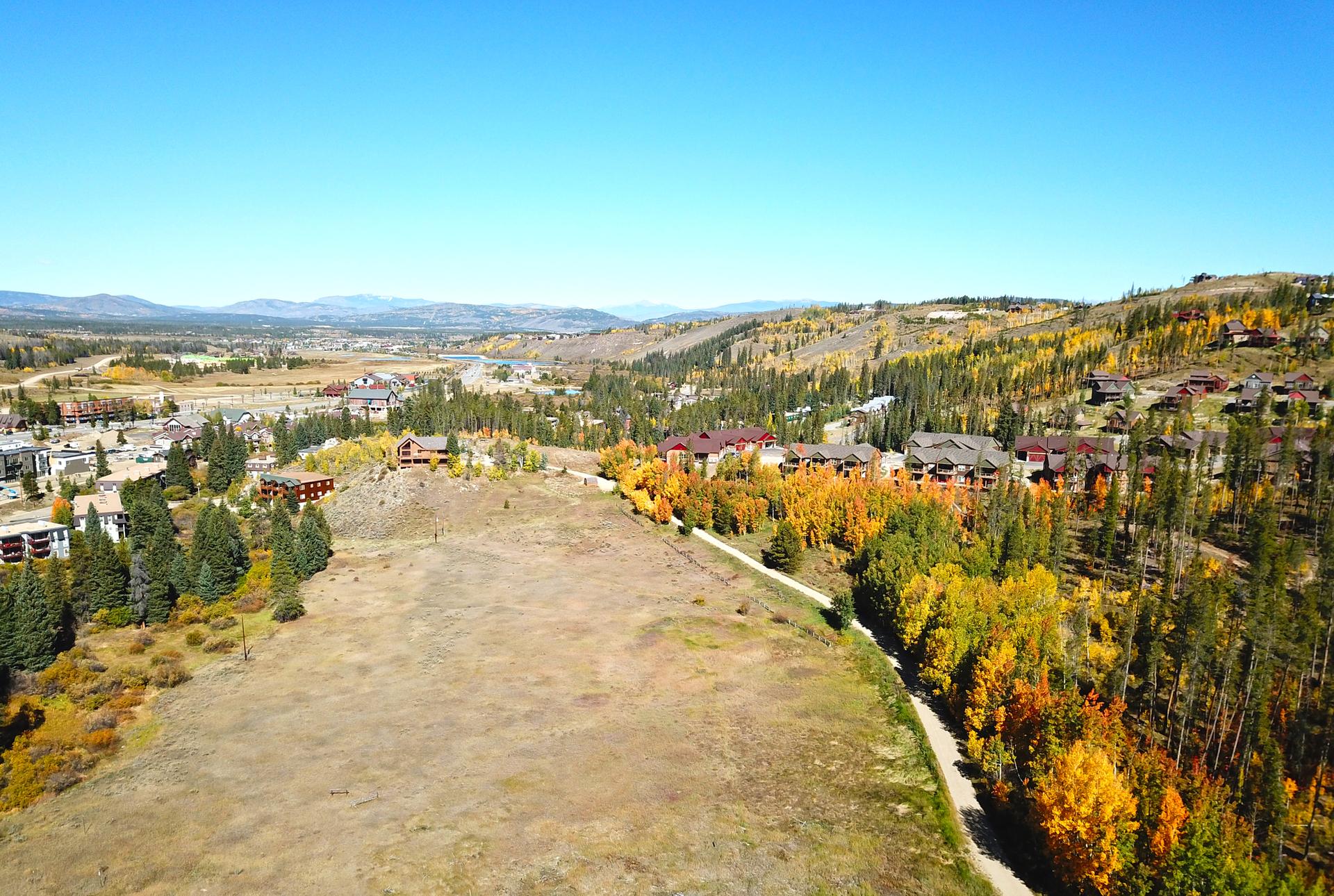 Aerial view of a valley with buildings and colorful autumn trees under blue sky.