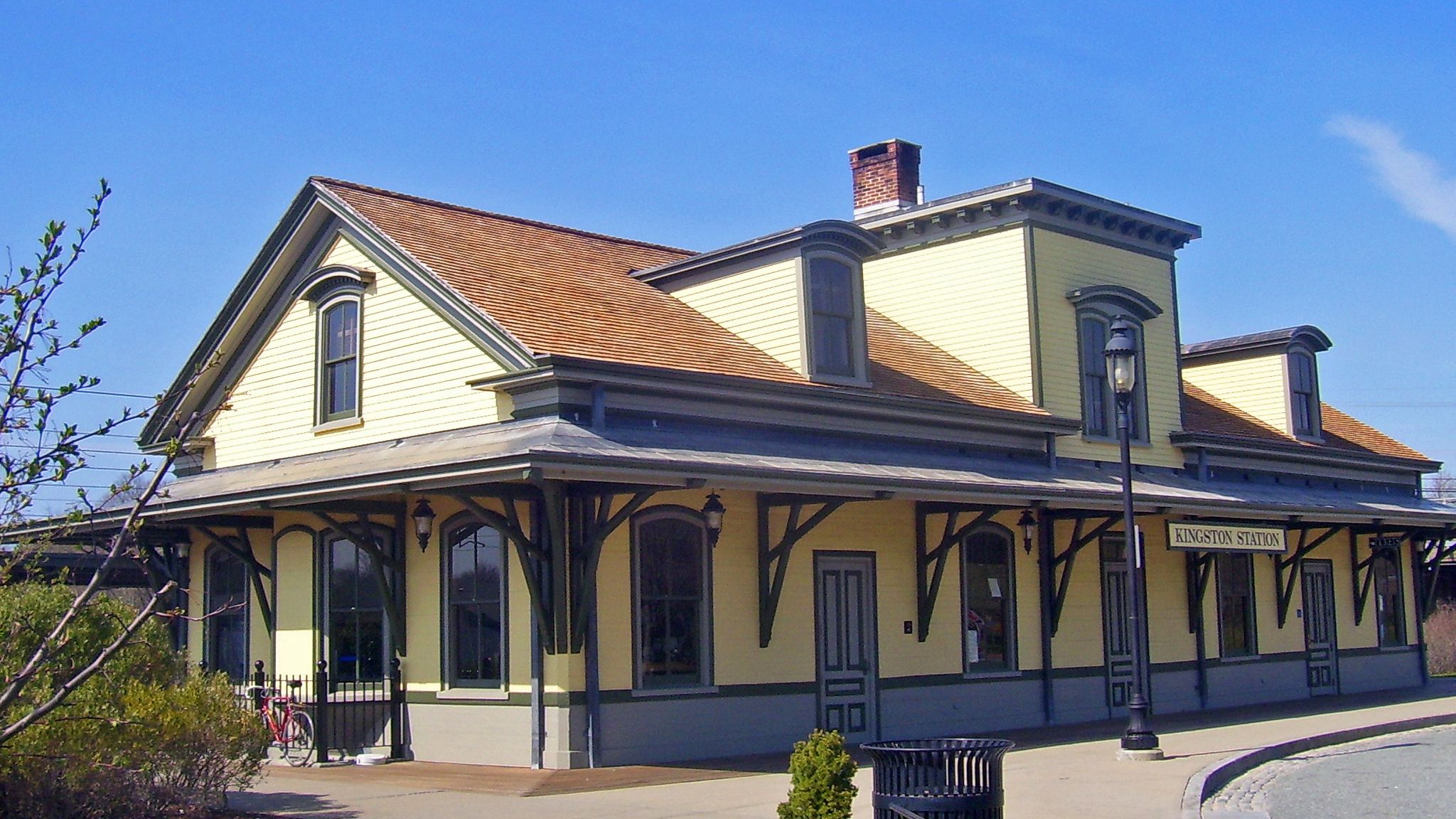 Historic yellow building with a brown roof and porch under a bright blue sky. - Round Rhody
