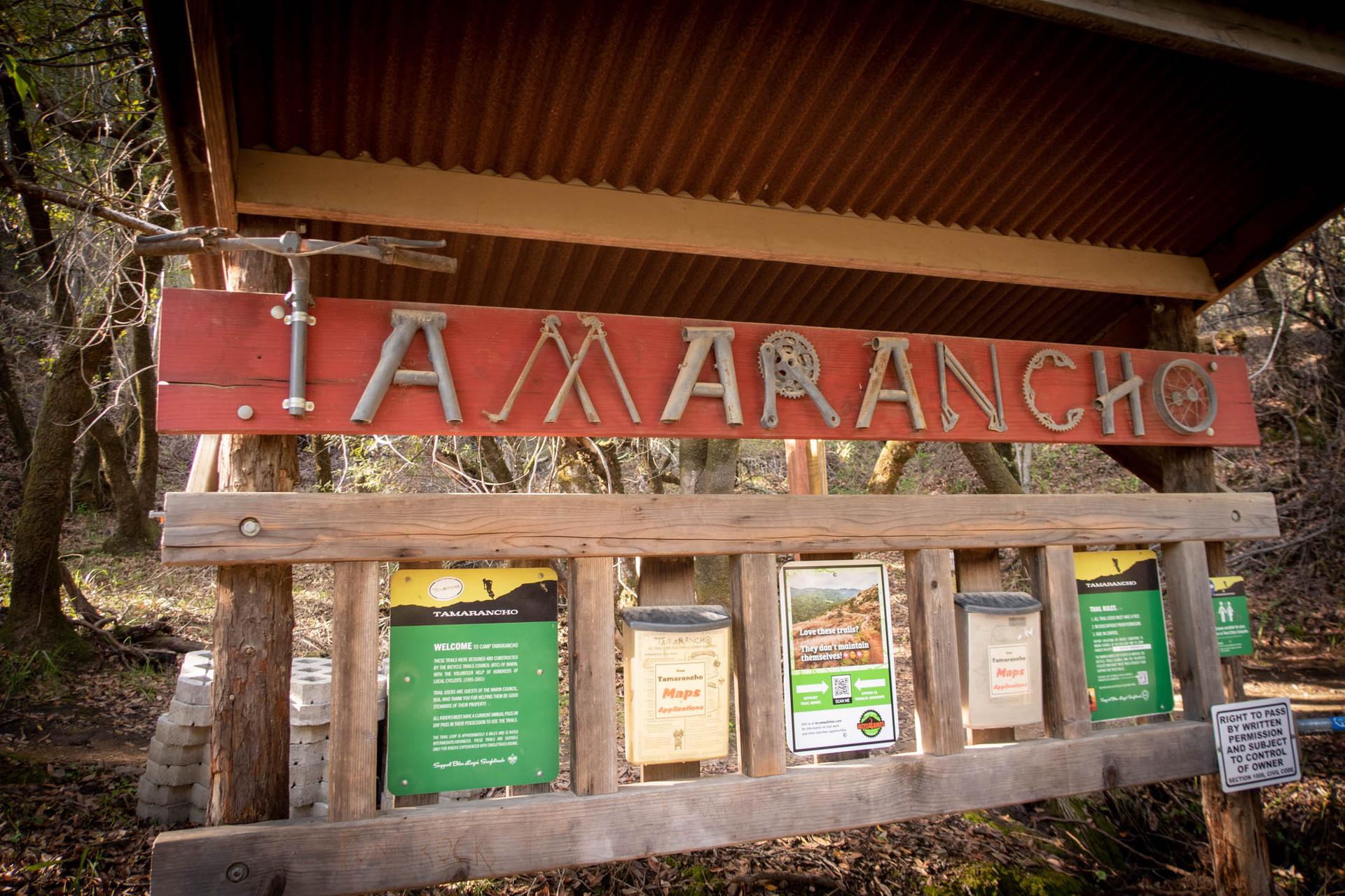 A rustic wooden sign with information boards in a shaded forest.